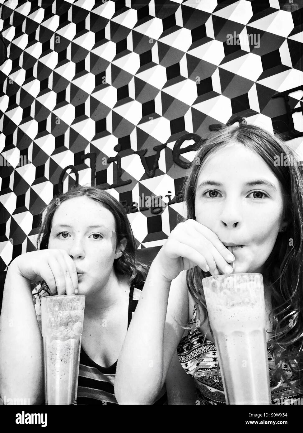 Two girls drinking milkshakes in cafe with geometric patterns on the wall - black and white Stock Photo