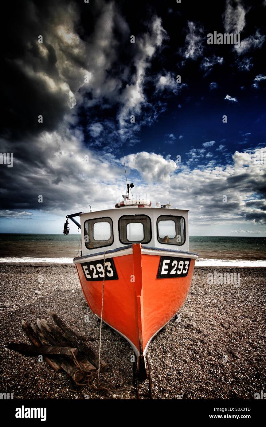 An old and unused fishing boat on a pebble beach and under a dramatic ...
