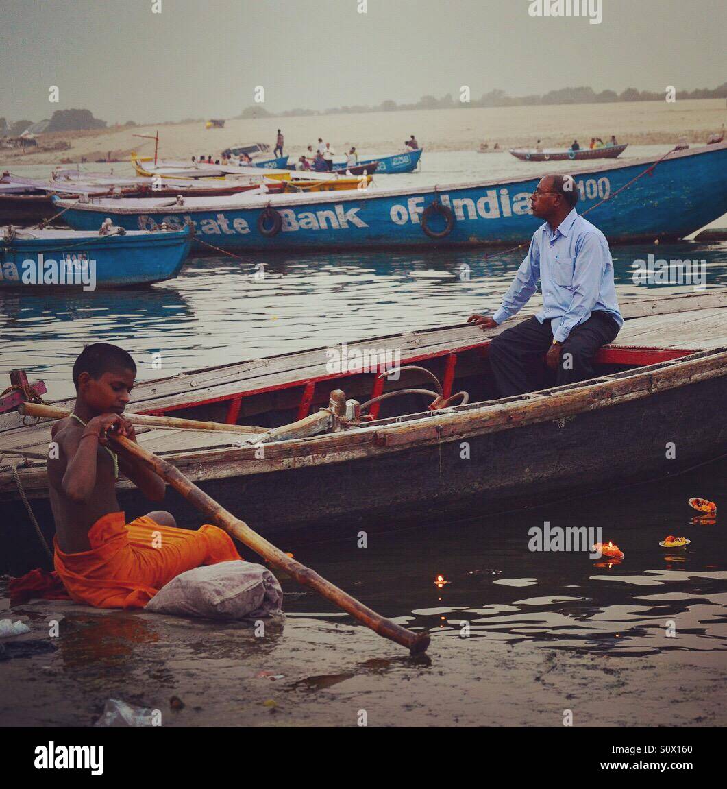 A boy in a playful mood and a man sitting on a boat on the banks of river Ganges in Varanasi, India Stock Photo