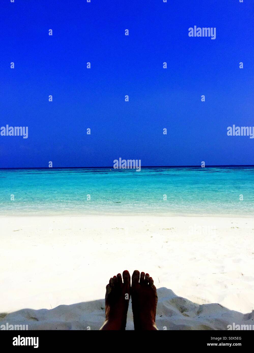 A pair of women's feet sunbathing on a tropical paradise beach in the Maldives - Smartphone Captured Stock Image