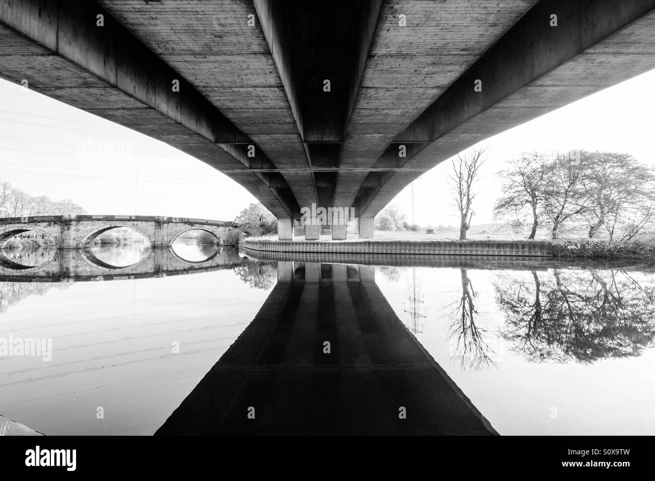 Below a modern bridge with an older bridge in the distance. Old and new bridges in black and white. - Smartphone Captured Stock Image