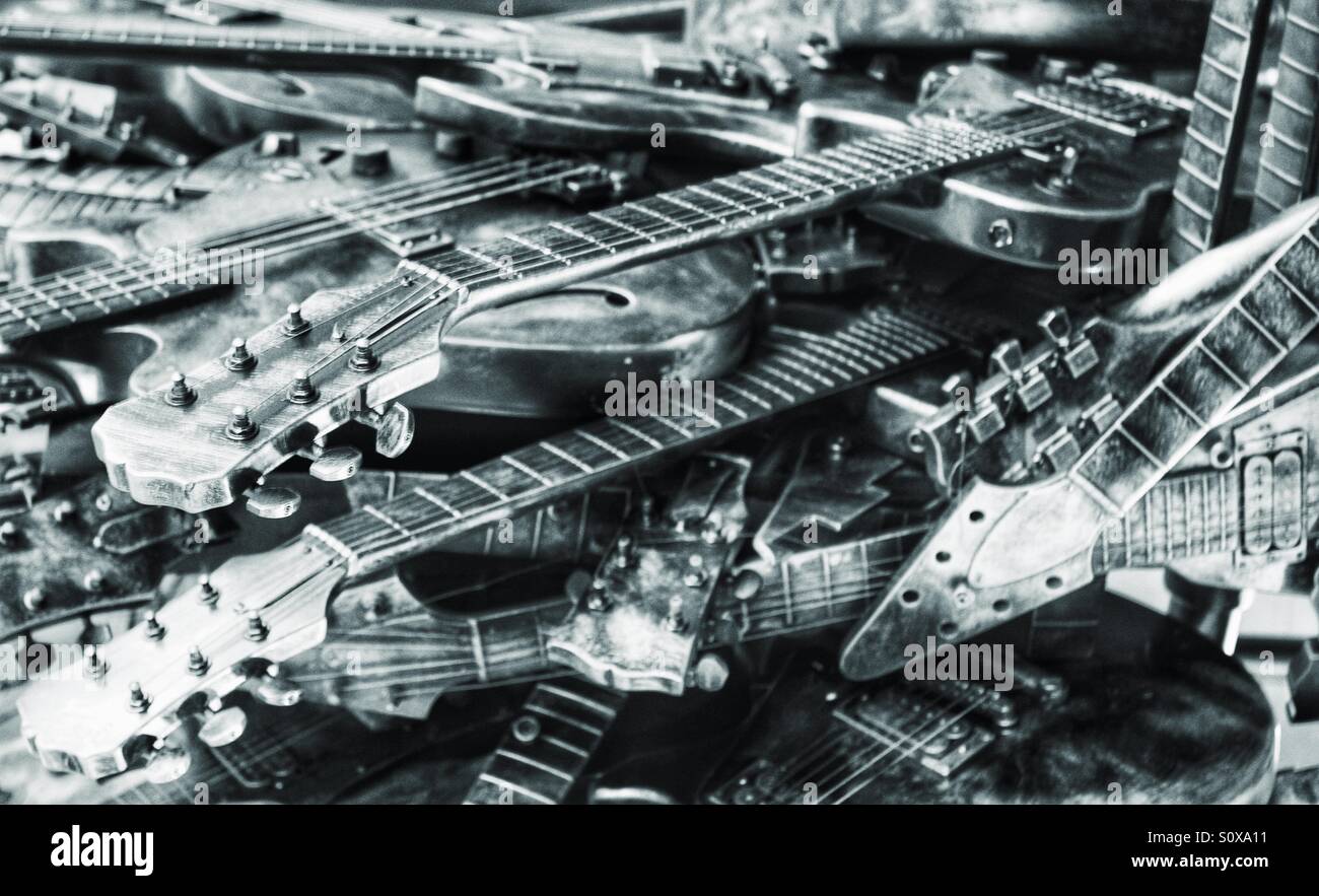 Discarded guitars in a messy pile. Black and white image with a metallic finish. Lots of guitars. Stock Photo