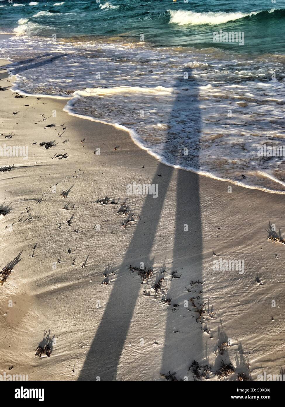 Long shadow of person walking along the beach in playa del Carmen Mexico as waves roll in - Smartphone Captured Stock Image