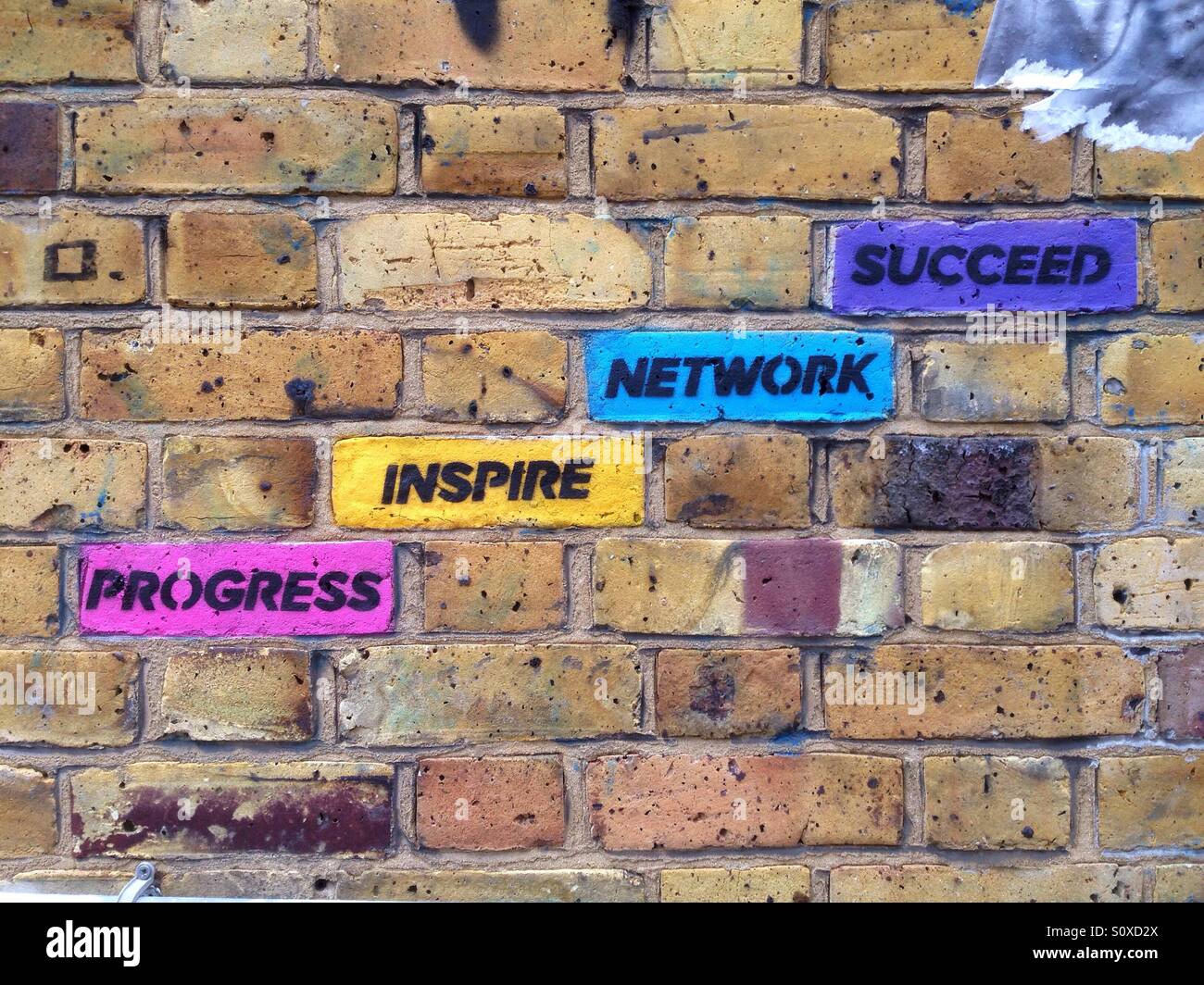 Street art in the area of Brick Lane, Shoreditch, East London, UK: coloured bricks with inspirational concepts progress, inspire, network, succeed - Smartphone Captured Stock Image