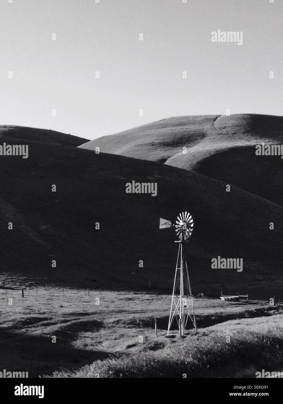 Windmill in hilly ranch country, in black and white Stock Photo