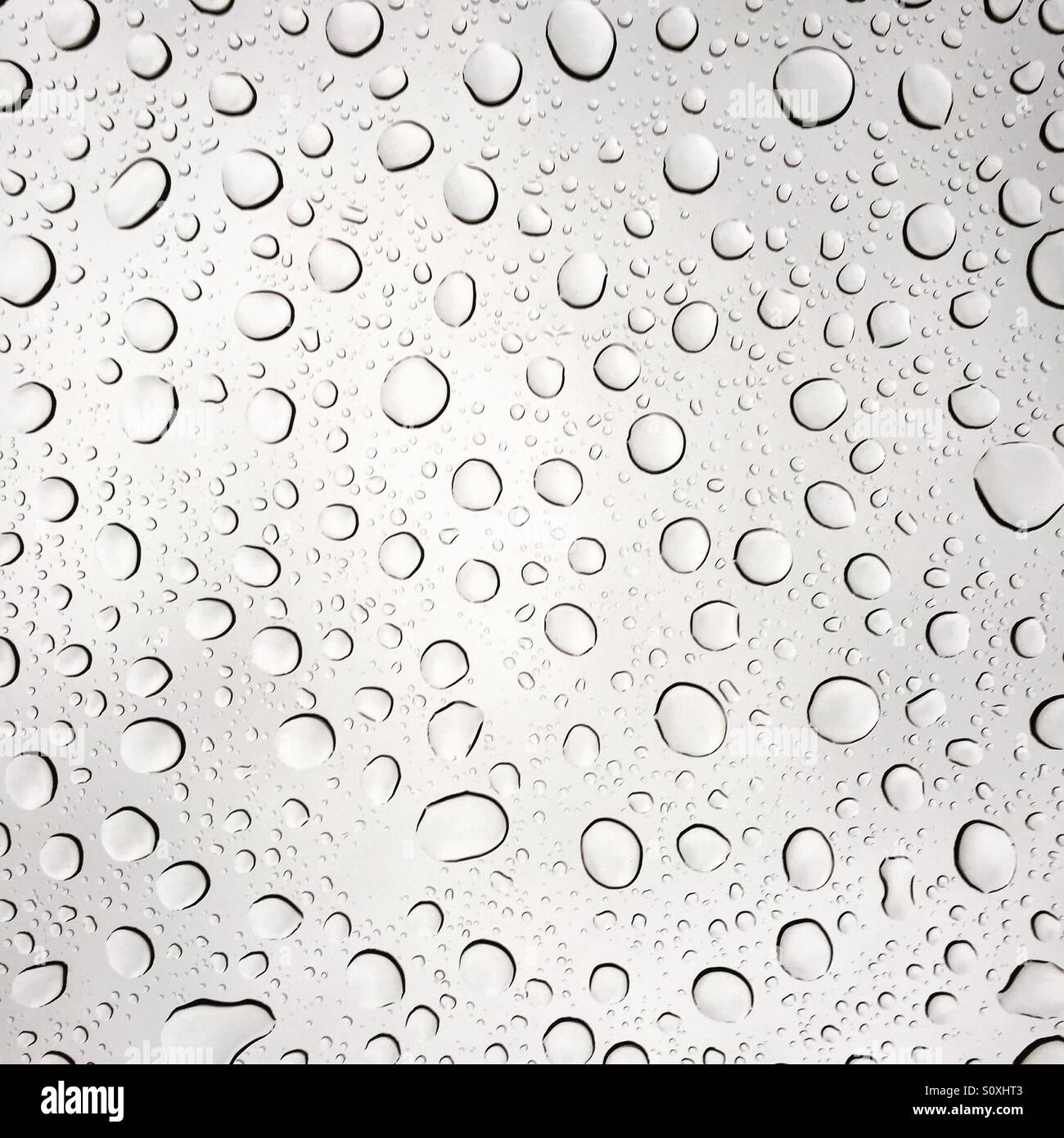 Raindrops on a clear glass pane, macro photography showing water droplets and light refractions on a window during rainfall. - Smartphone Captured Stock Image