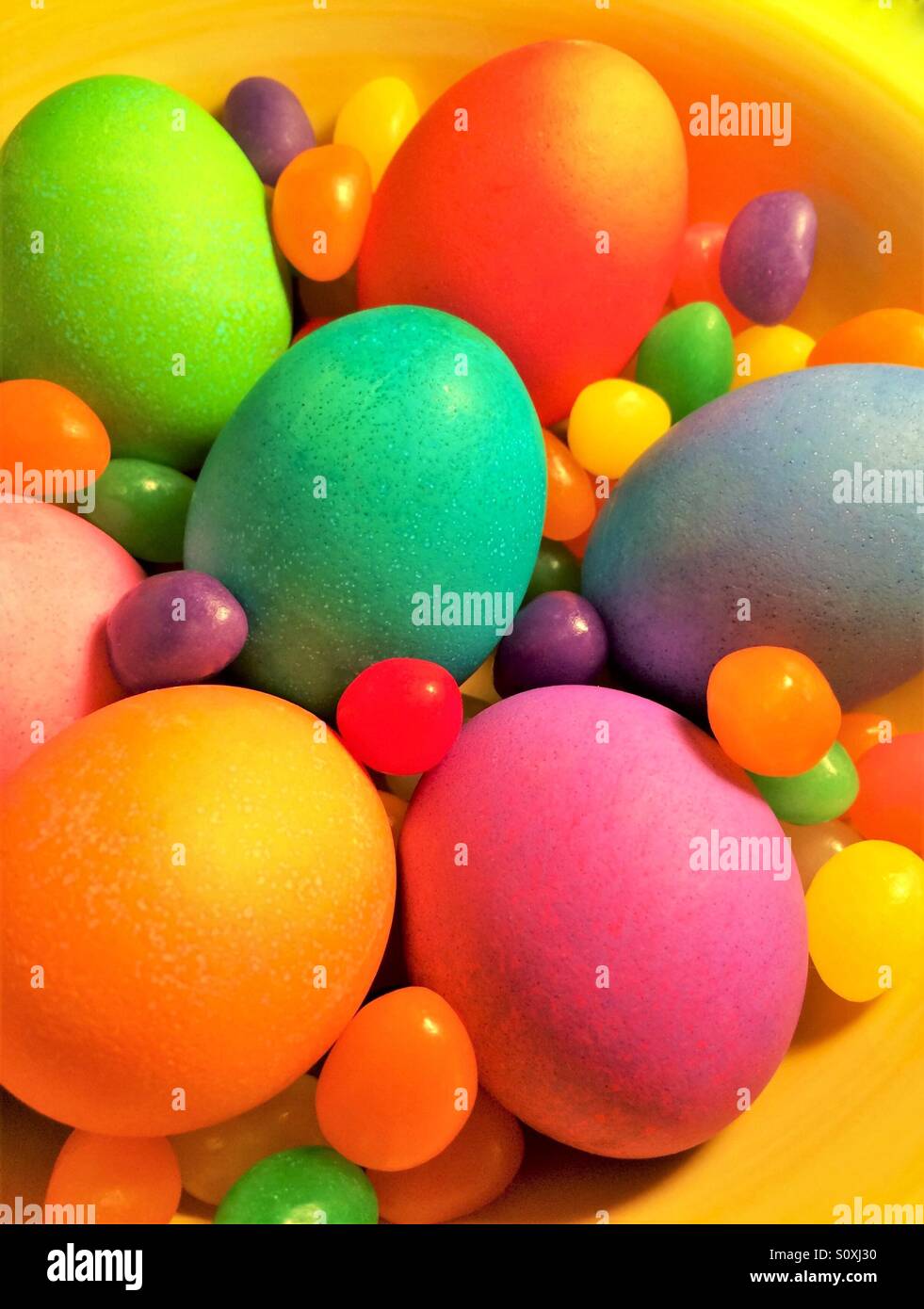 Colored eggs and jelly beans in a yellow bowl Stock Photo