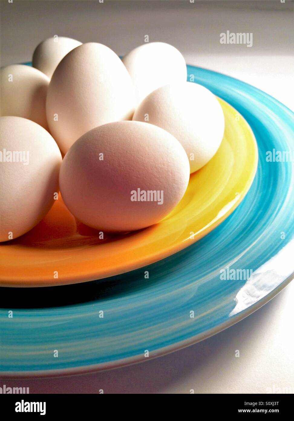 Whole white eggs on colorful plates side lit close-up view - Smartphone Captured Stock Image