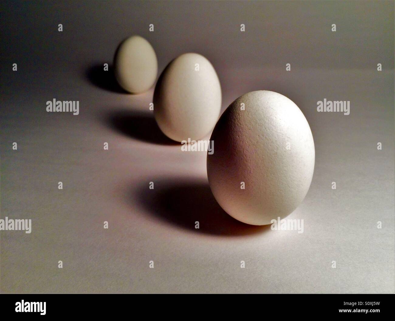 Three eggs standing upright side lit with dramatic shadows on white background - Smartphone Captured Stock Image