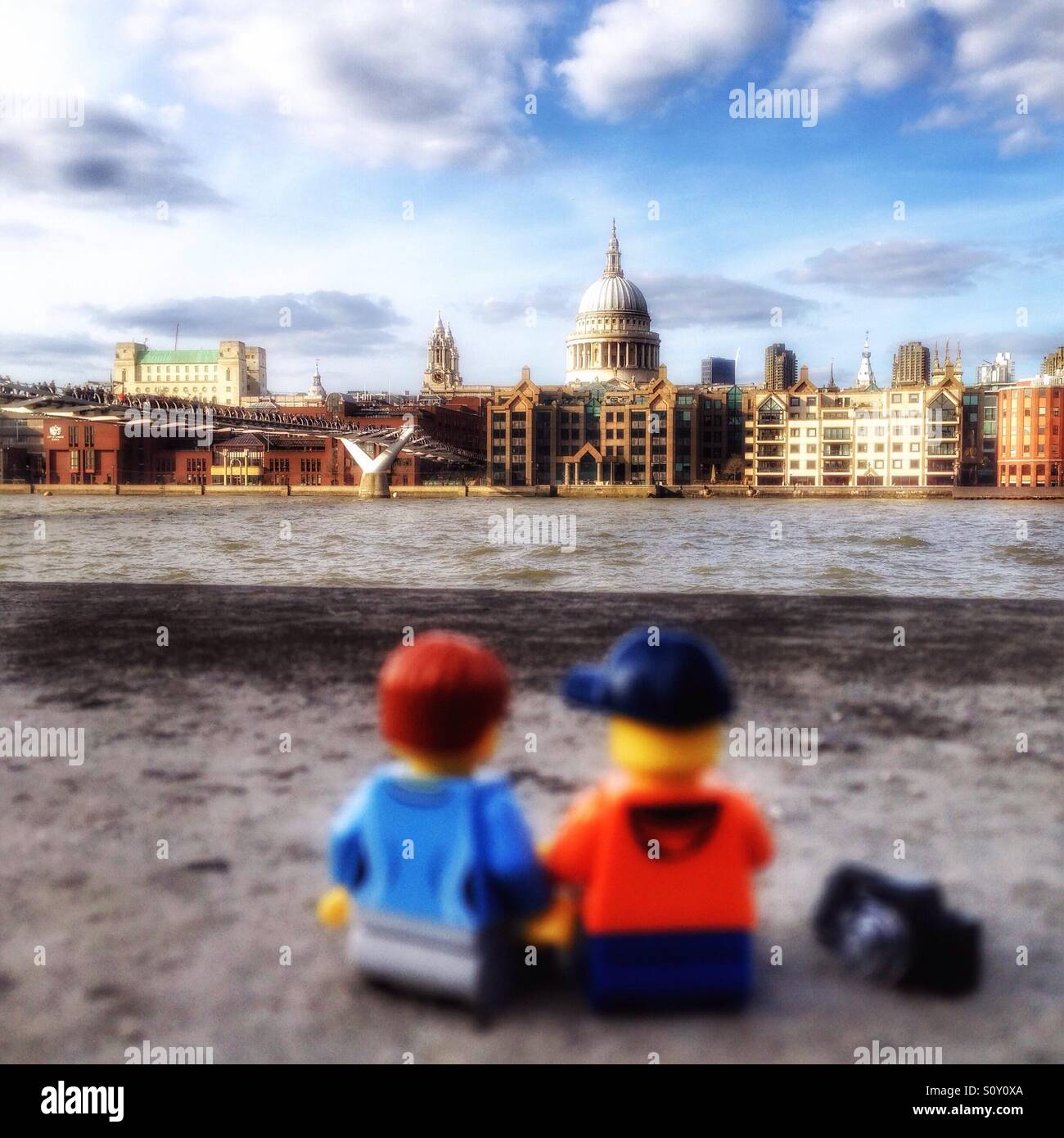 A Lego couple sitting at the River Thames looking at the London skyline with St Paul and The Millennium Bridge Stock Photo