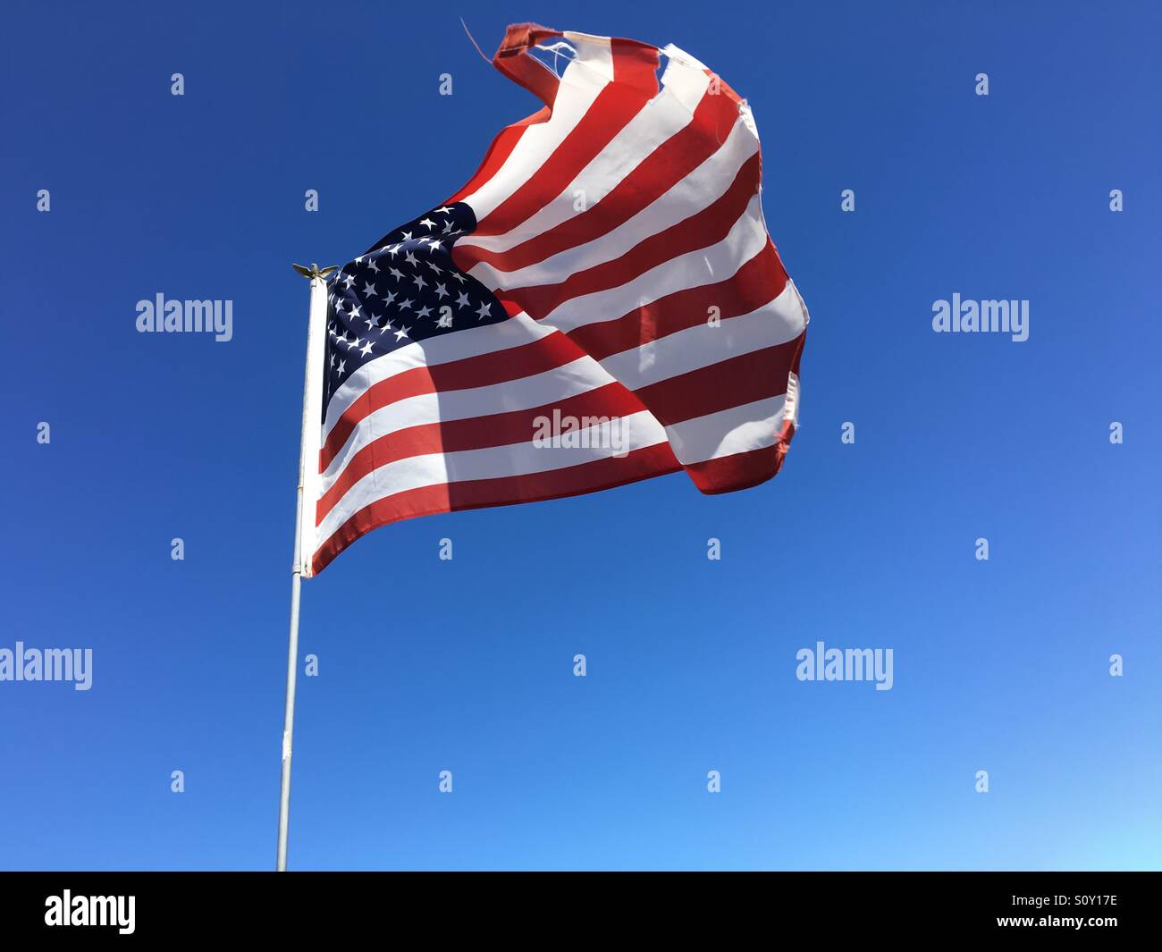 A tattered American flag flying against a clear blue sky - Smartphone Captured Stock Image