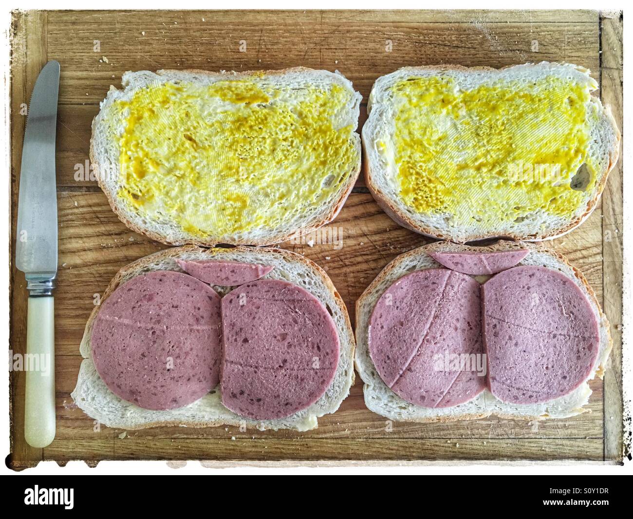 Liver sausage sandwiches with kitchen knife resting on a old wooden cutting board. Viewed from above. Stock Photo