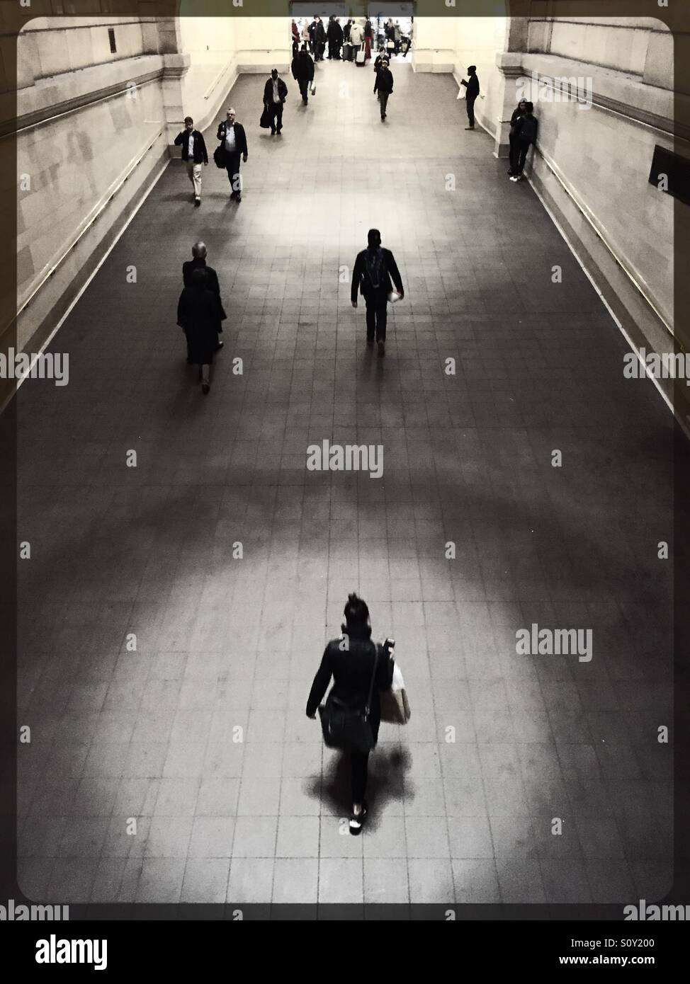 Lone woman traveler is highlighted walking up a ramp, Grand Central terminal, New York City. - Smartphone Captured Stock Image