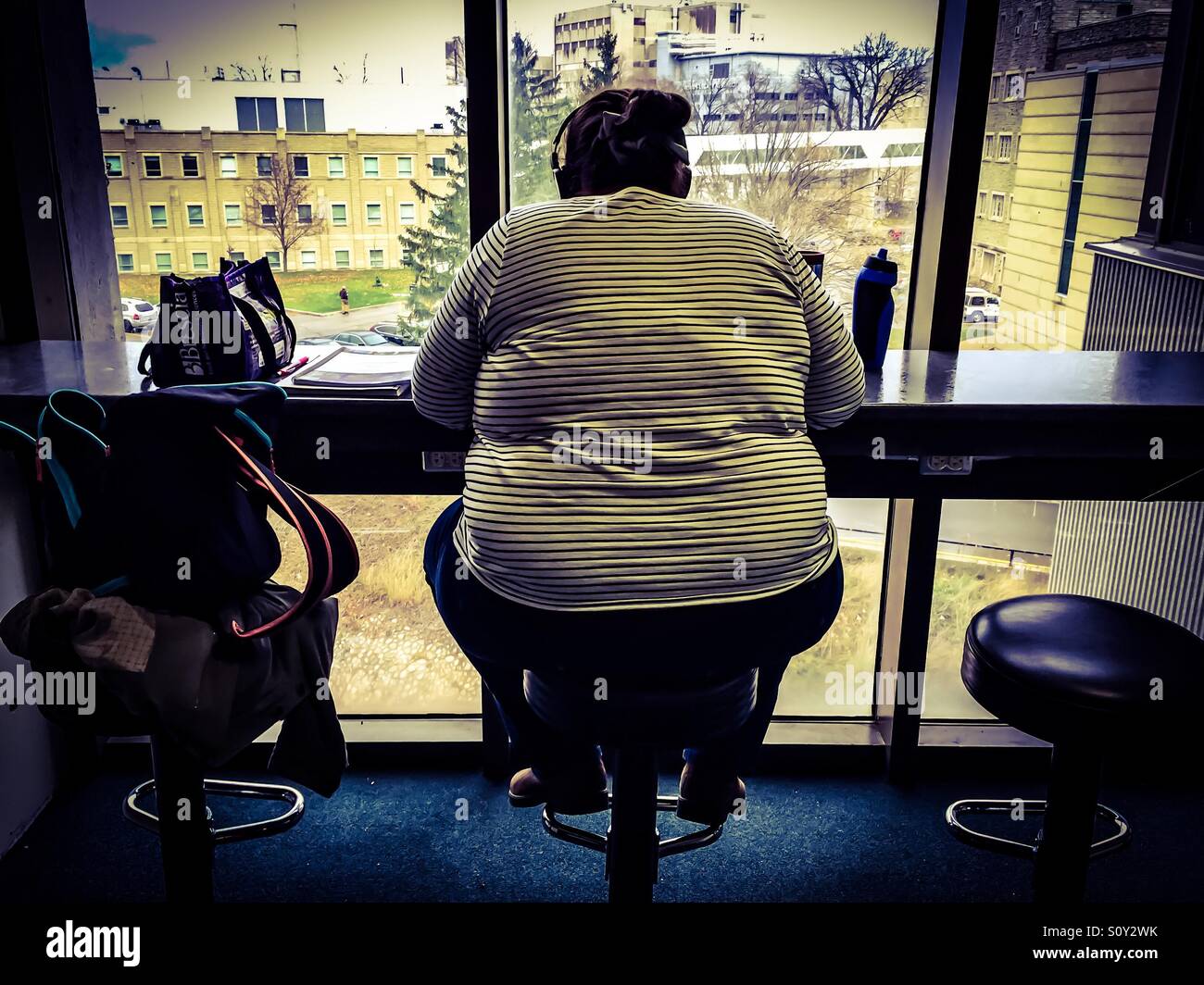 Overweight man with headphones sitting at a counter of a café looking out on the street, Ontario, Canada. - Smartphone Captured Stock Image