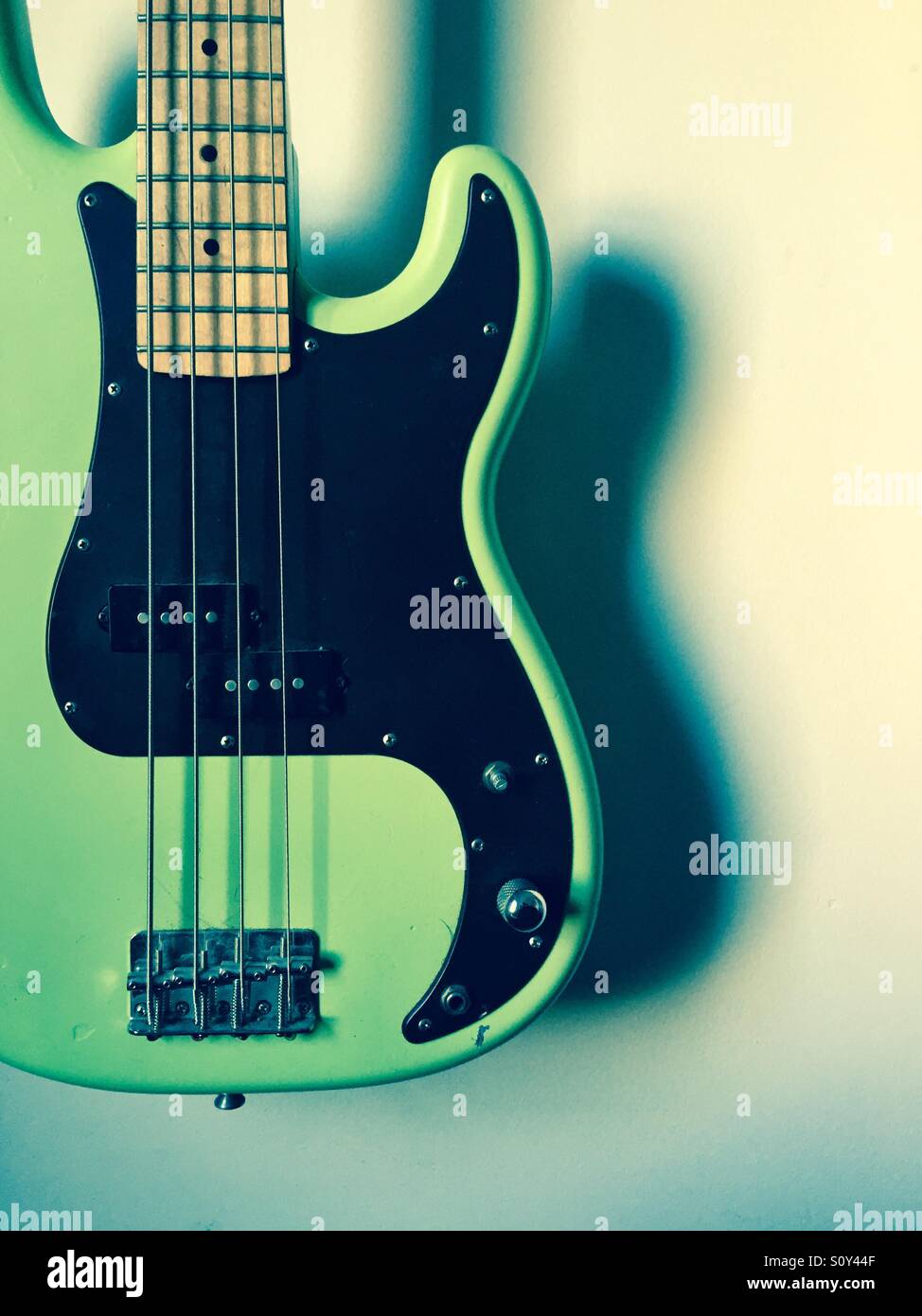 Green four string bass guitar hanging offset on white wall Stock Photo