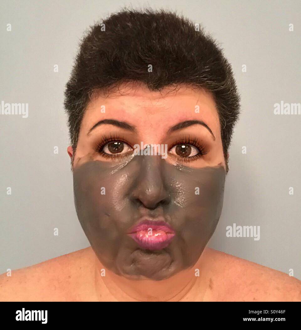 A dark haired woman has a mud mask on and is pursing her lips comically. - Smartphone Captured Stock Image