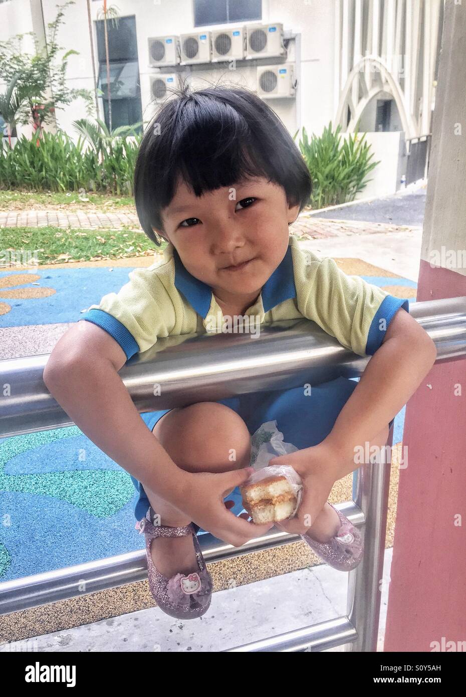Delightful 4year old Singapore girl squatting on the fence telling mom what she is doing Stock Photo