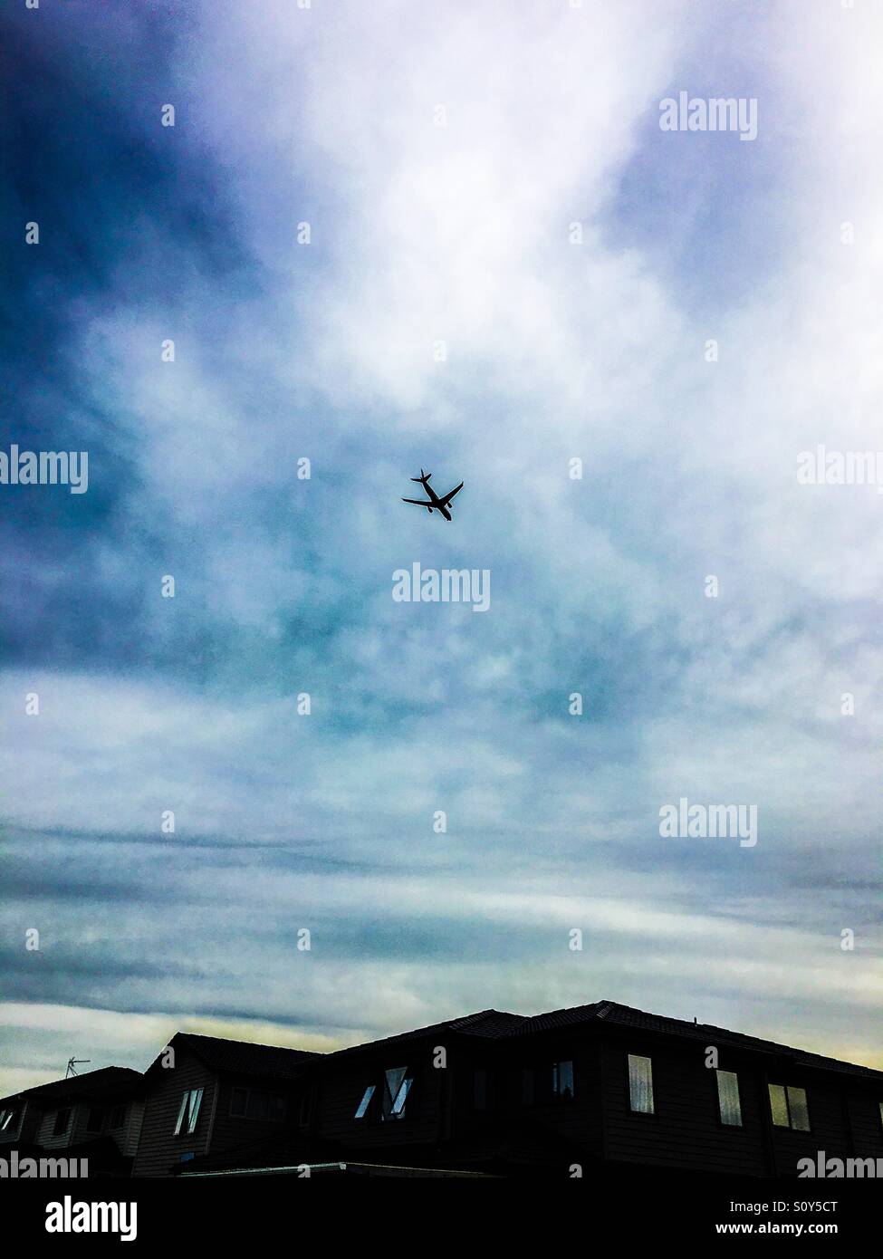 Airplane flying over the house roofs Stock Photo