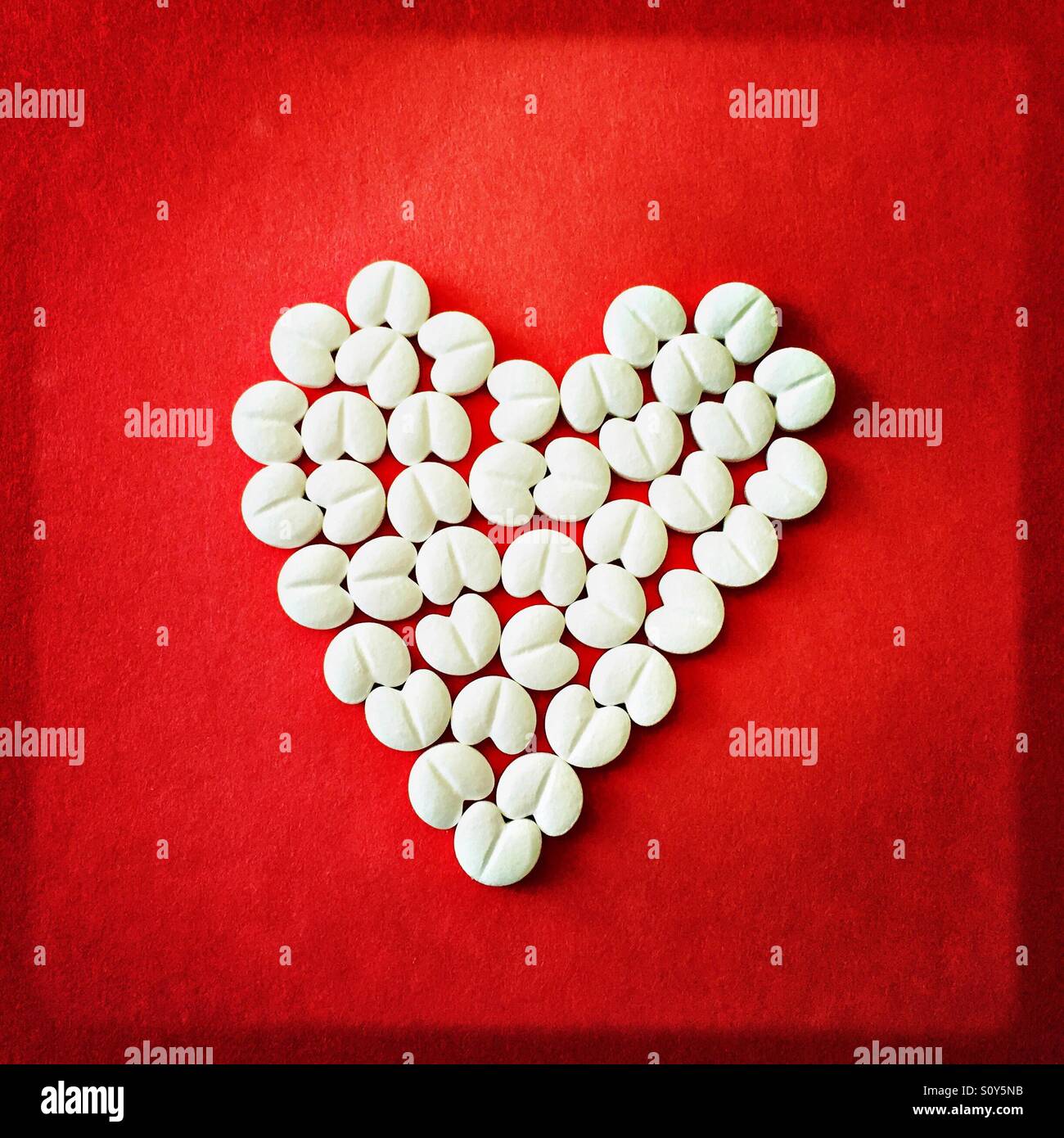 Heart-shaped tablets on red background - Smartphone Captured Stock Image