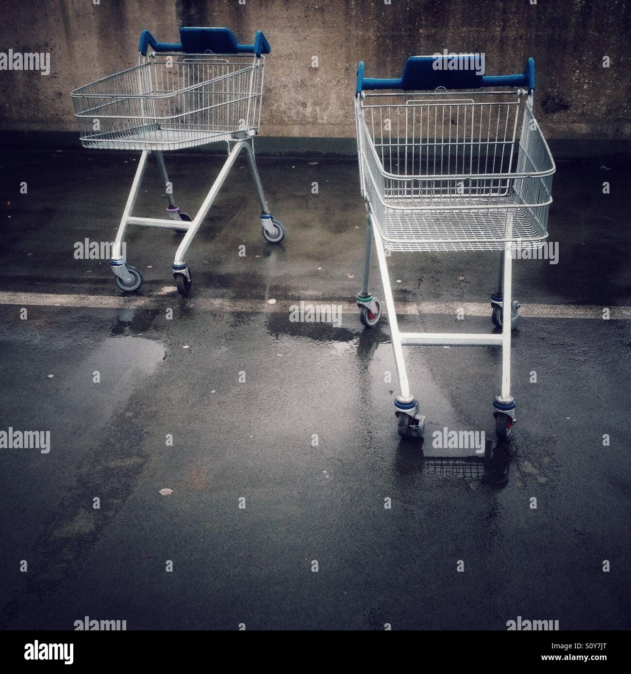 Two empty shopping trollies or carts in a wet car park. - Smartphone Captured Stock Image