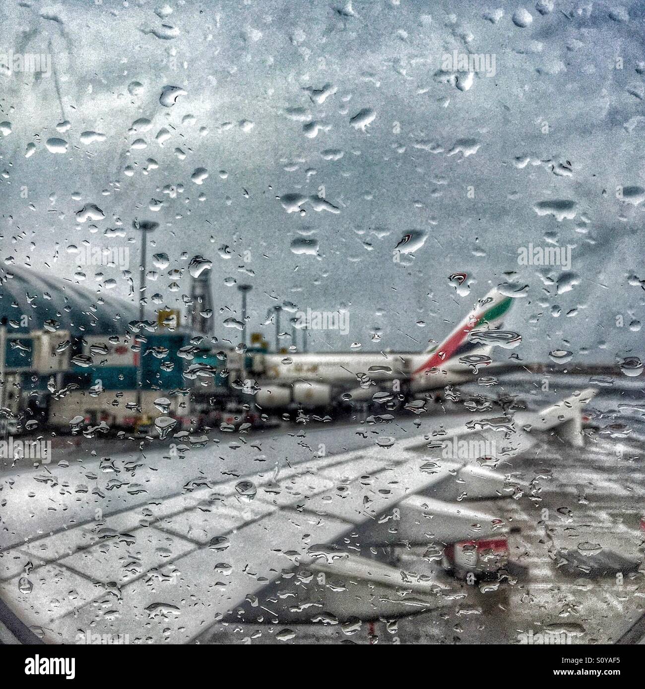 Parked Emirates Airline's plane seen through the rainy aircraft window at Dubai International Airport Stock Photo