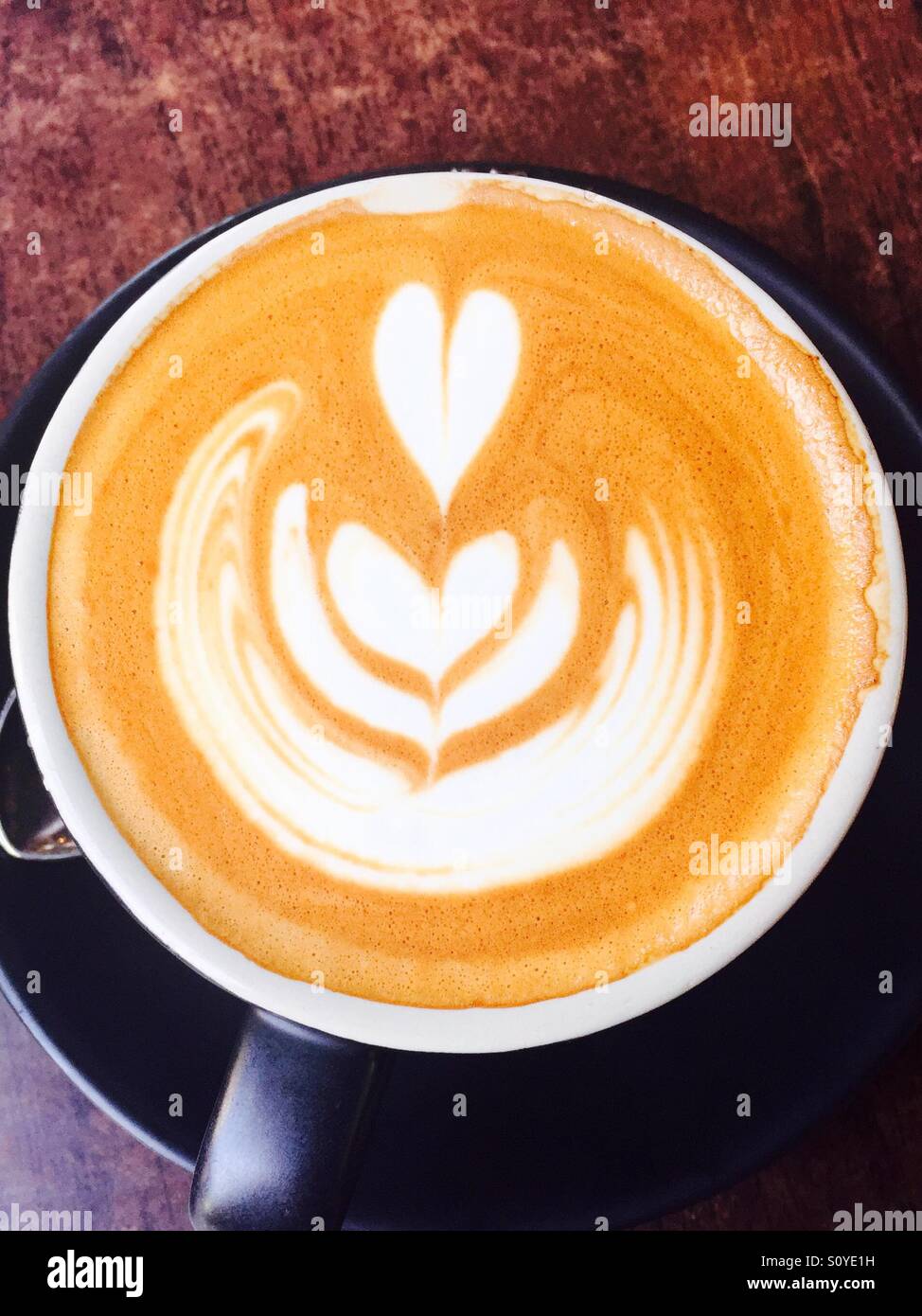 Coffee in black cup with heart foam shapes  on coffee cream - Smartphone Captured Stock Image