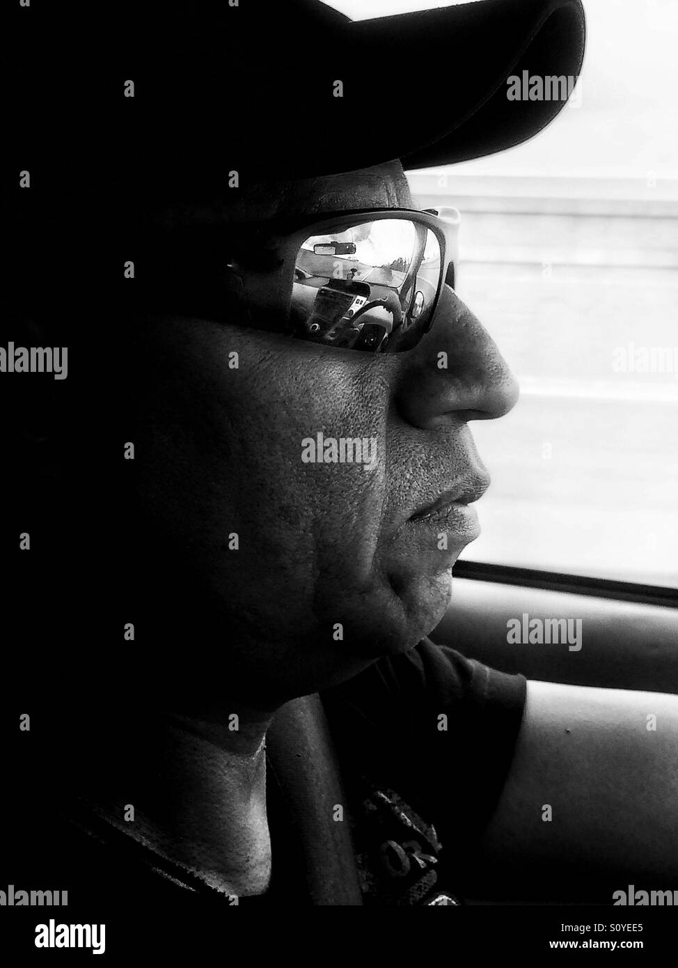 Portrait of middle aged Hispanic man driving with sunglasses and baseball cap. Stock Photo