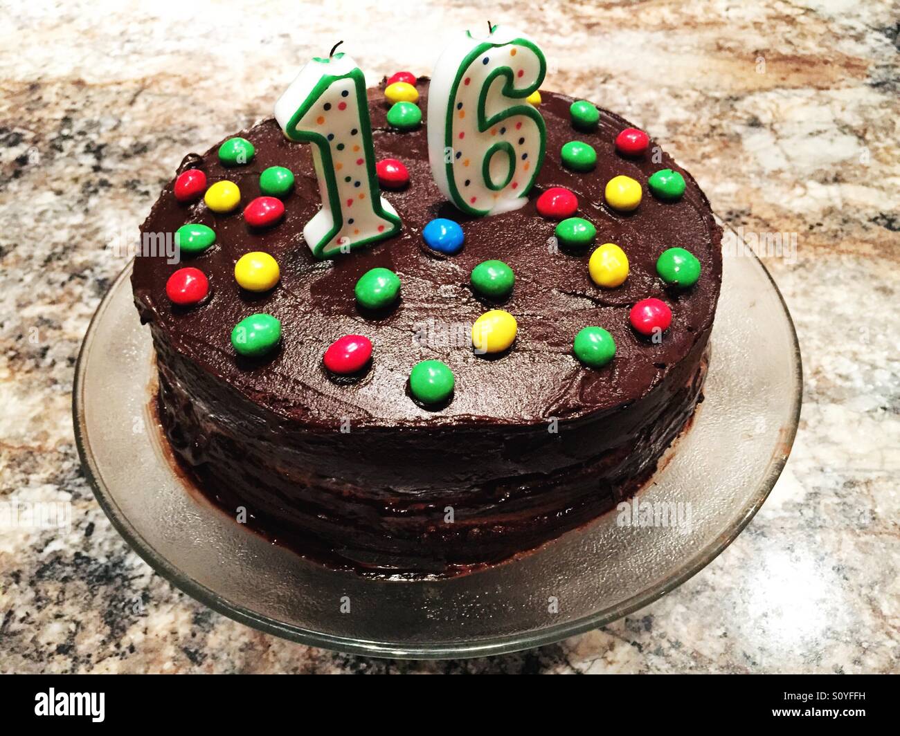 Home baked chocolate cake with chocolate frosting topped with colorful candy and candles - Smartphone Captured Stock Image