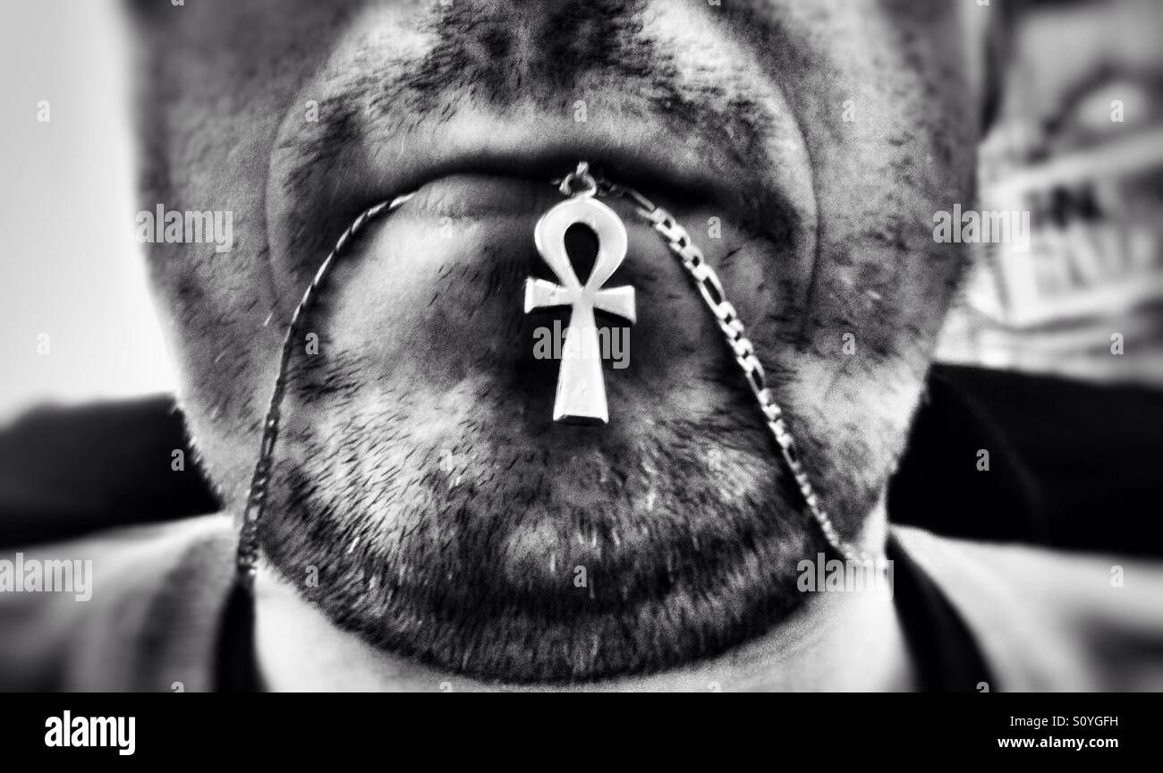 A man with stubble chewing on his necklace. - Smartphone Captured Stock Image