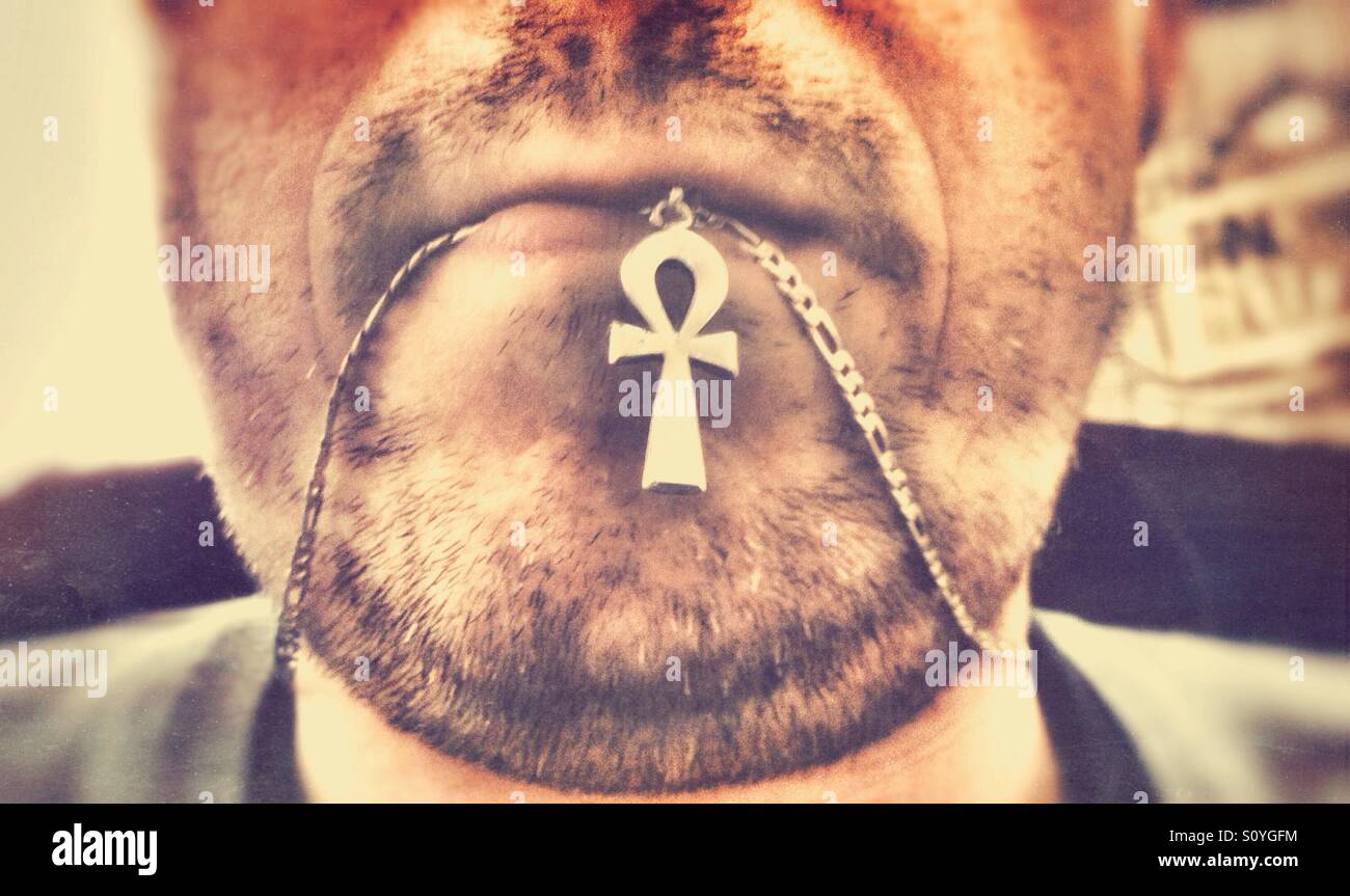 A man with stubble chewing on his necklace. - Smartphone Captured Stock Image