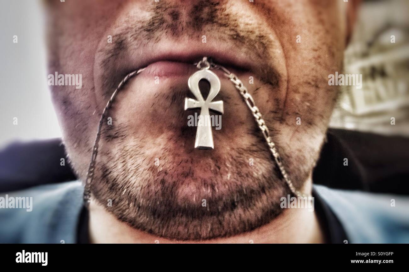 A man with stubble chewing on his necklace. - Smartphone Captured Stock Image