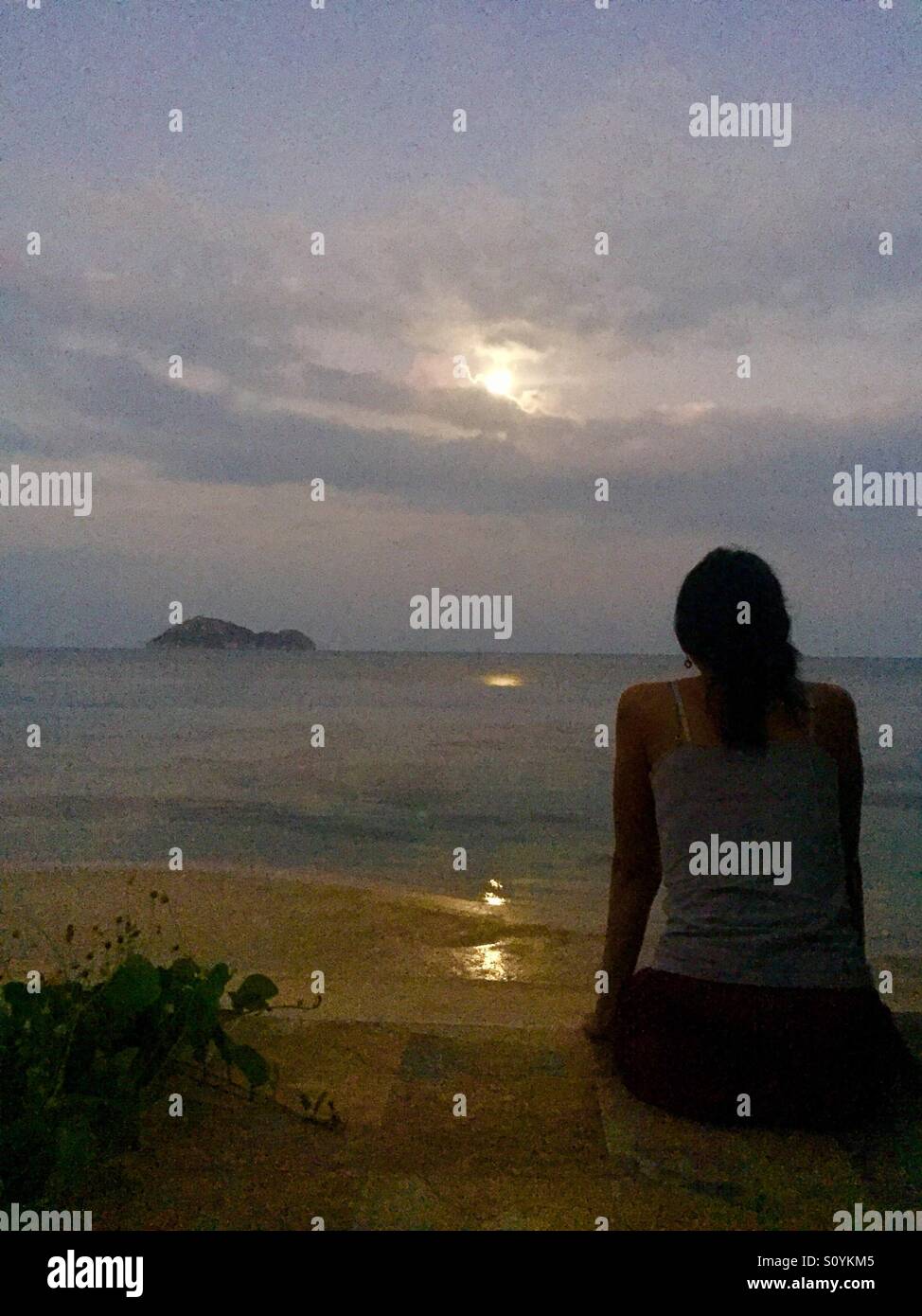 My friend Nueng watches the moon, just as the break of dawn sets on the island of Koh Phangan in Thailand. Stock Photo