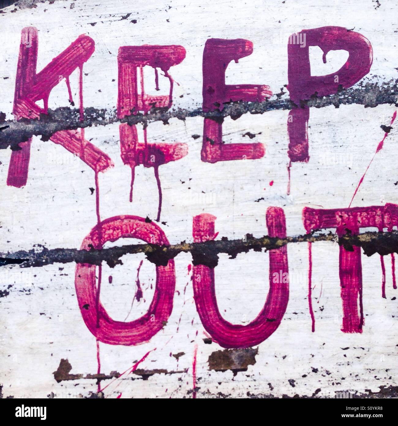 Keep Out sign written in red dripping paint, a little bit like blood, on a white, whitewashed wood beamed fence. Stock Photo