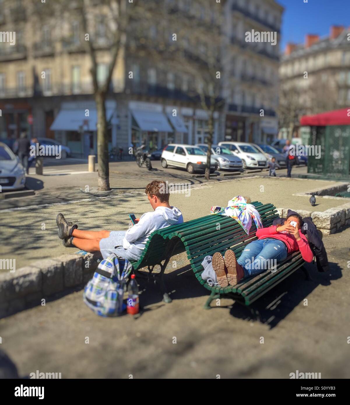 Two persons using smartphones sitting on a bench in the park, Grenoble,France - Smartphone Captured Stock Image