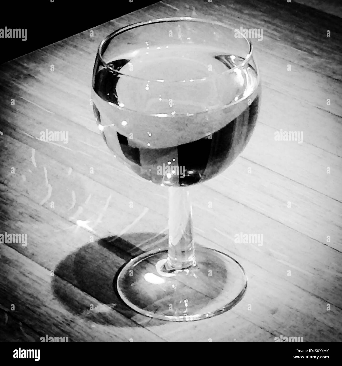 Black and white photograph of a glass of wine on a wooden table - Smartphone Captured Stock Image