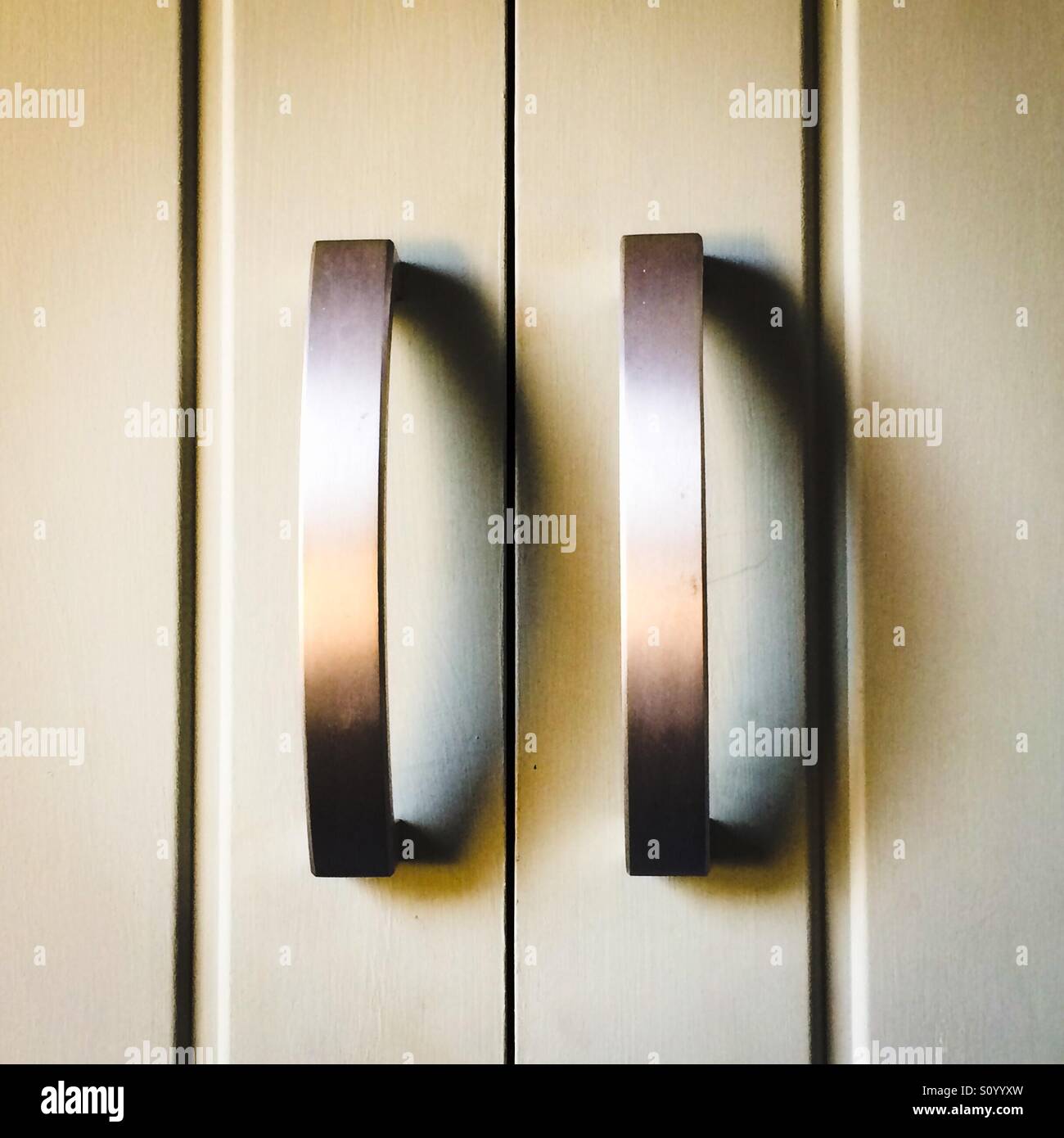 Close up view of a pair of metal door handles on a wooden cupboard - Smartphone Captured Stock Image