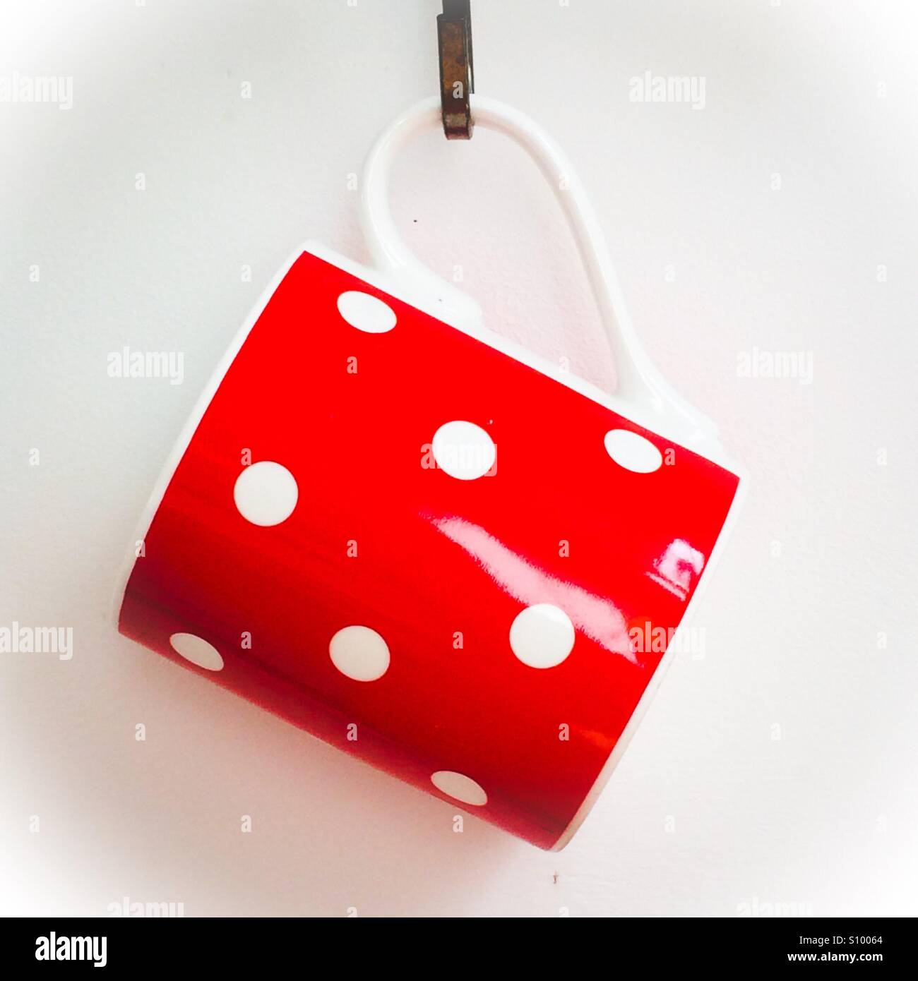 Red mug with white spots hanging on a hook Stock Photo