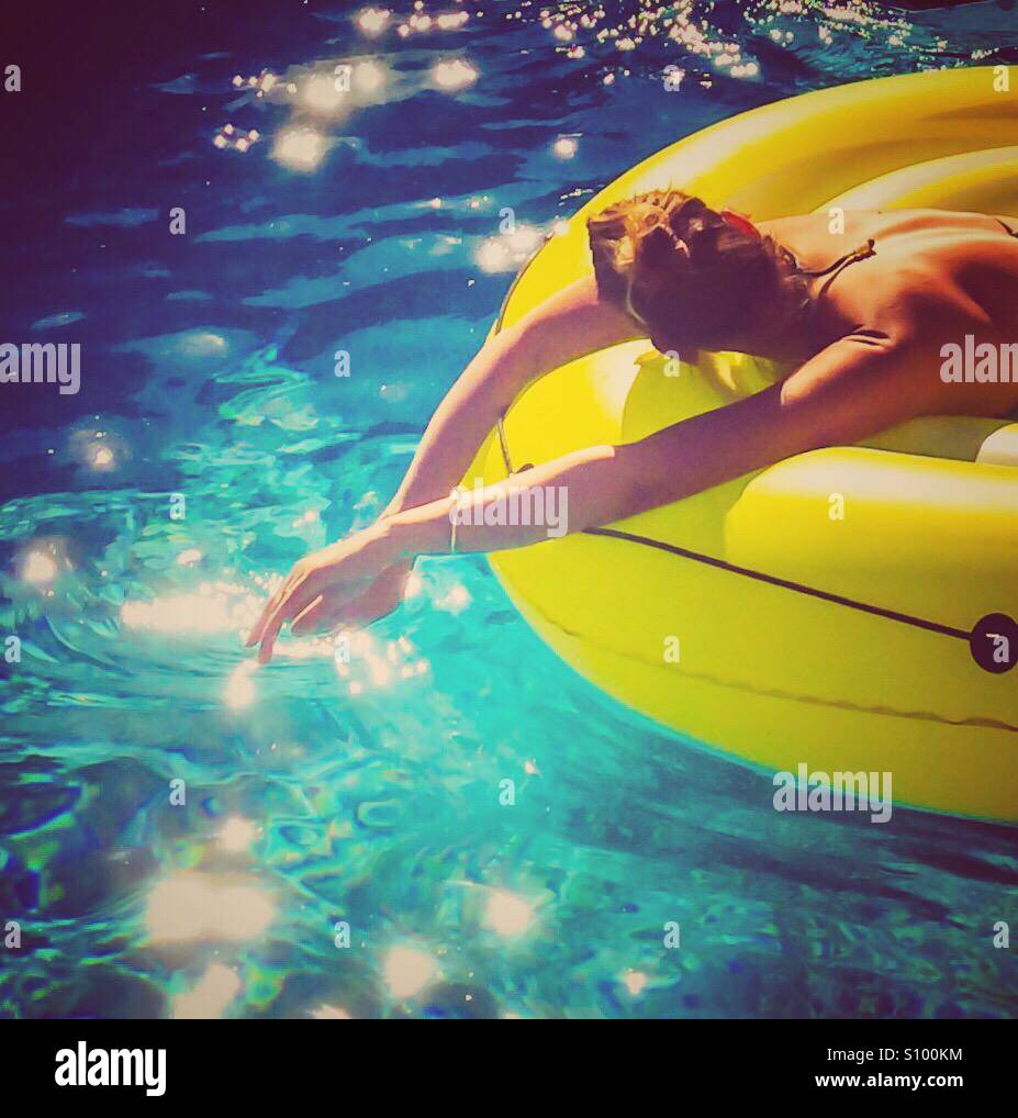 Woman relaxing on an inflatable mat floating in blue waters on a sunny hot day. Stock Photo