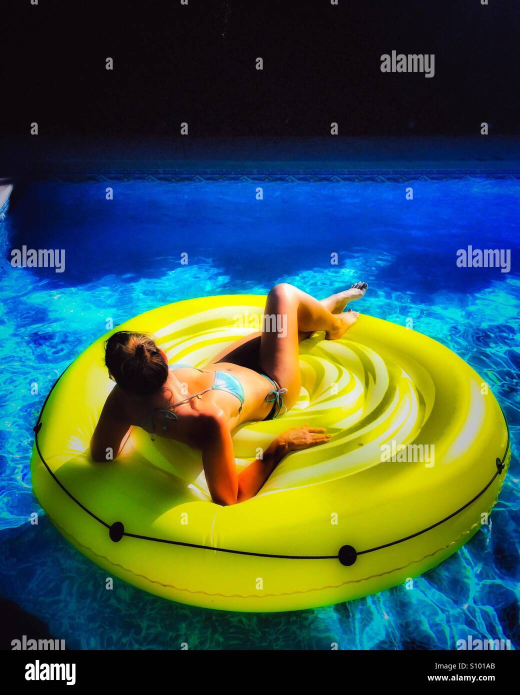 Woman relaxing on an inflatable mat in a pool on a sunny day. Stock Photo