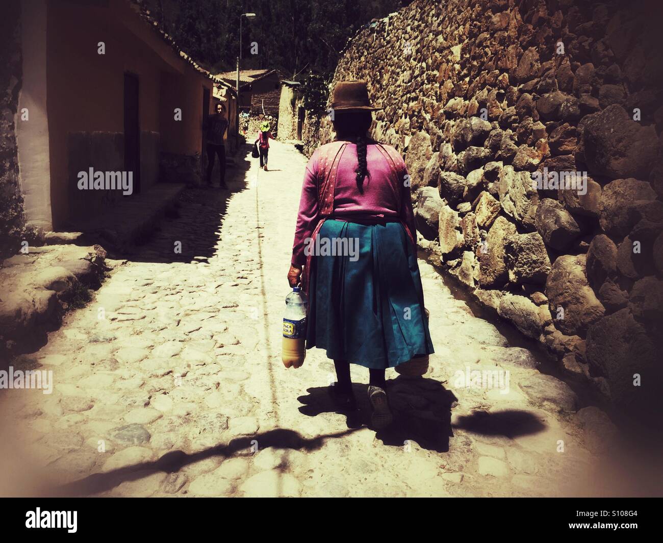 Peruvian woman in traditional clothes walking home with groceries in ancient city of Ollantaytambo - Smartphone Captured Stock Image