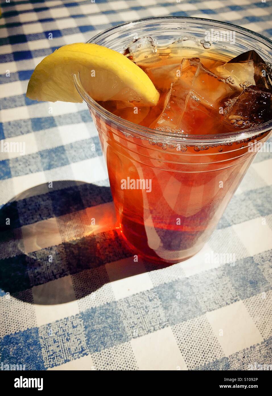 Iced tea with lemon slice served in plastic cup on blue and white checked tablecloth. - Smartphone Captured Stock Image