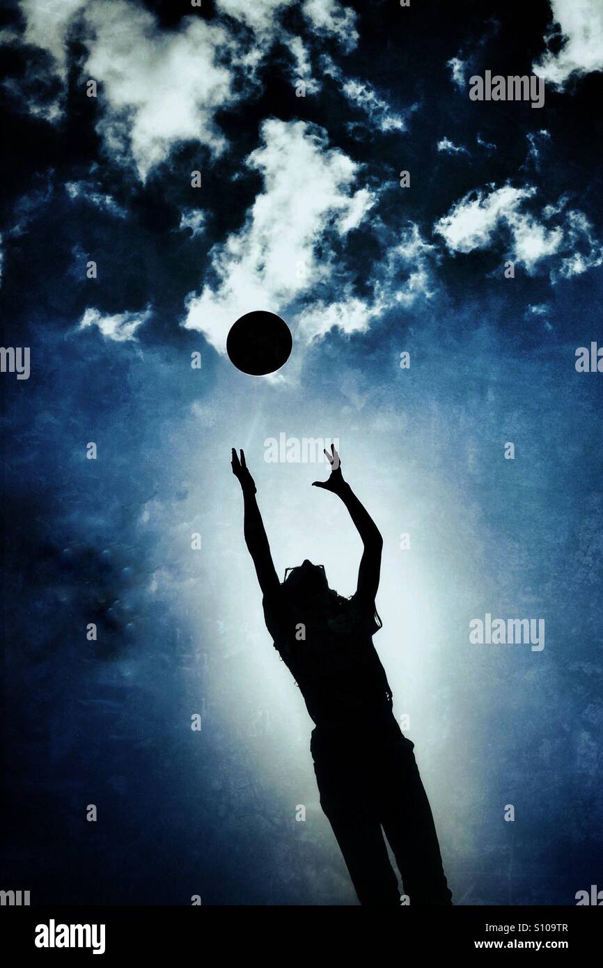 Young girl playing catch with football in silhouette against dramatic sky Stock Photo