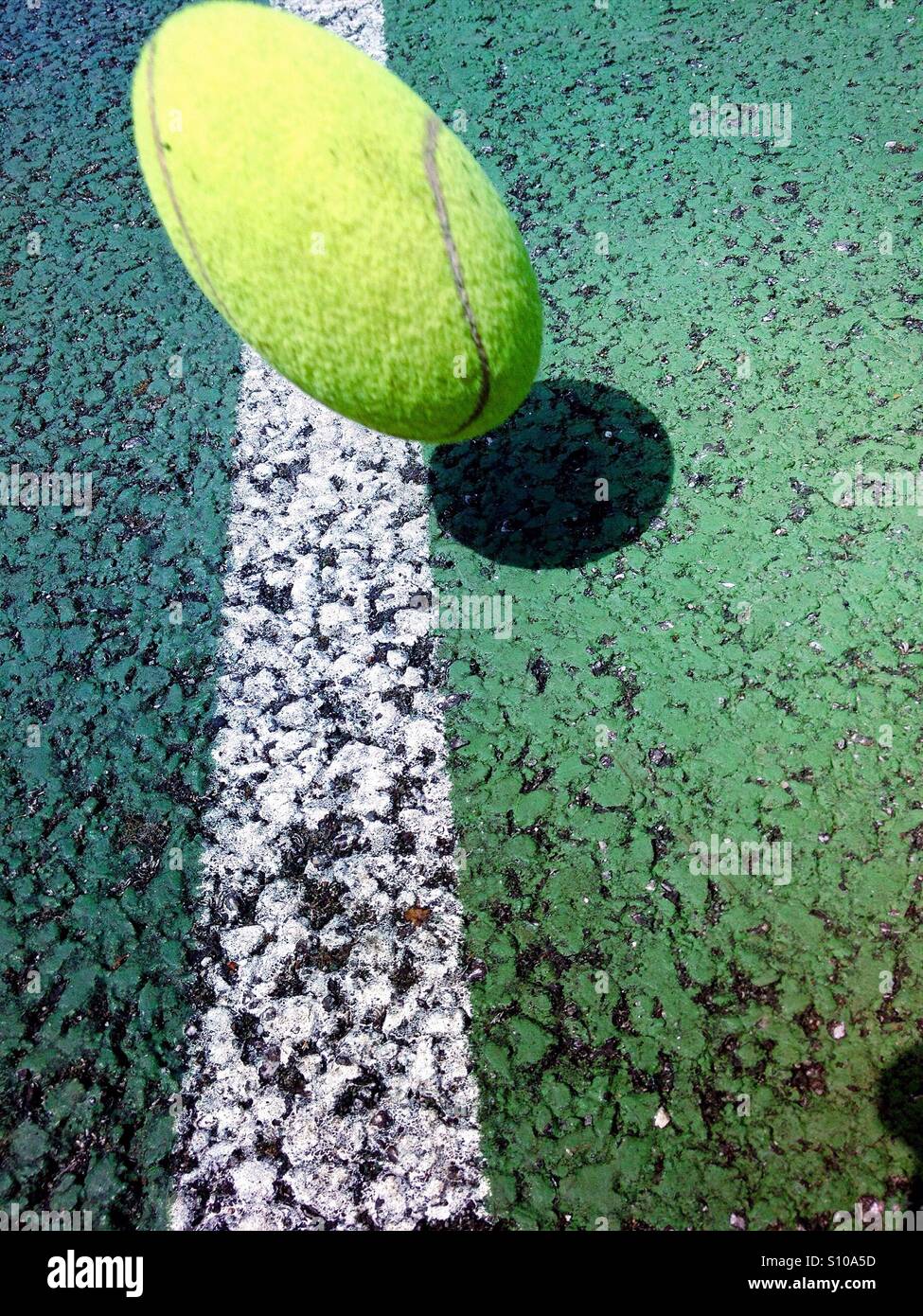 Moving tennis ball about to fall on the line of a tennis court Stock Photo