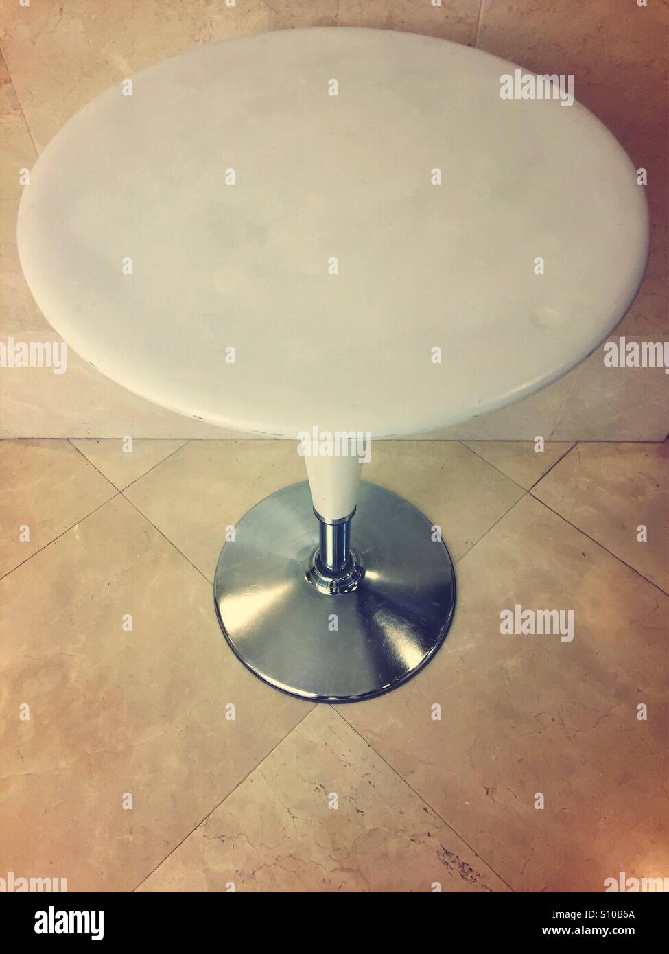 Round empty white Bombo table standing on a tiled floor against a wall - Smartphone Captured Stock Image