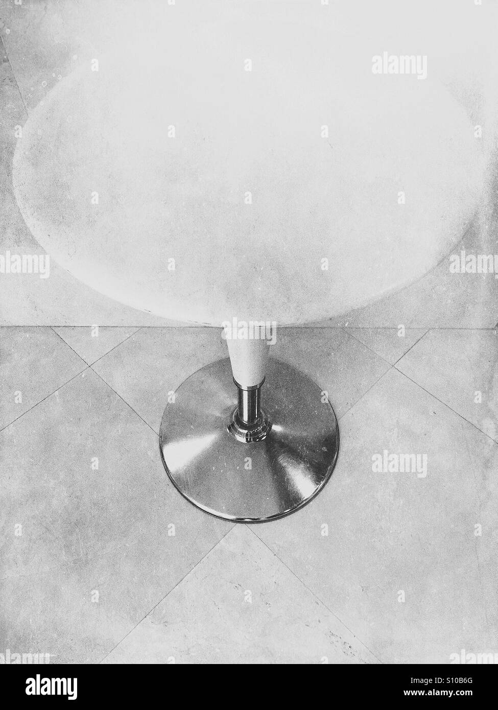 Round white empty Bombo table standing on a tiled floor against a wall - Smartphone Captured Stock Image