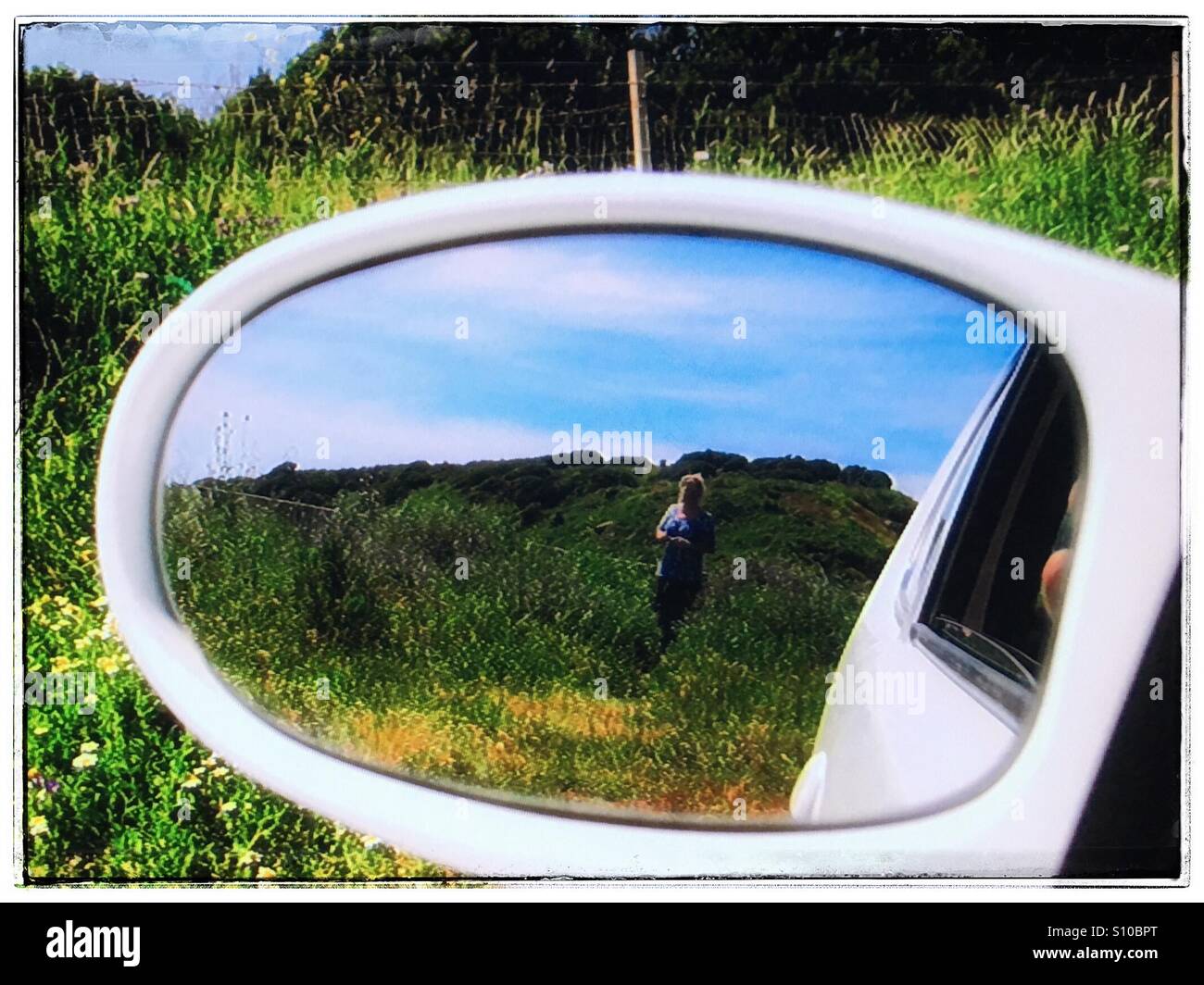 Woman walking in a field as seen through a side mirror of a car Stock Photo