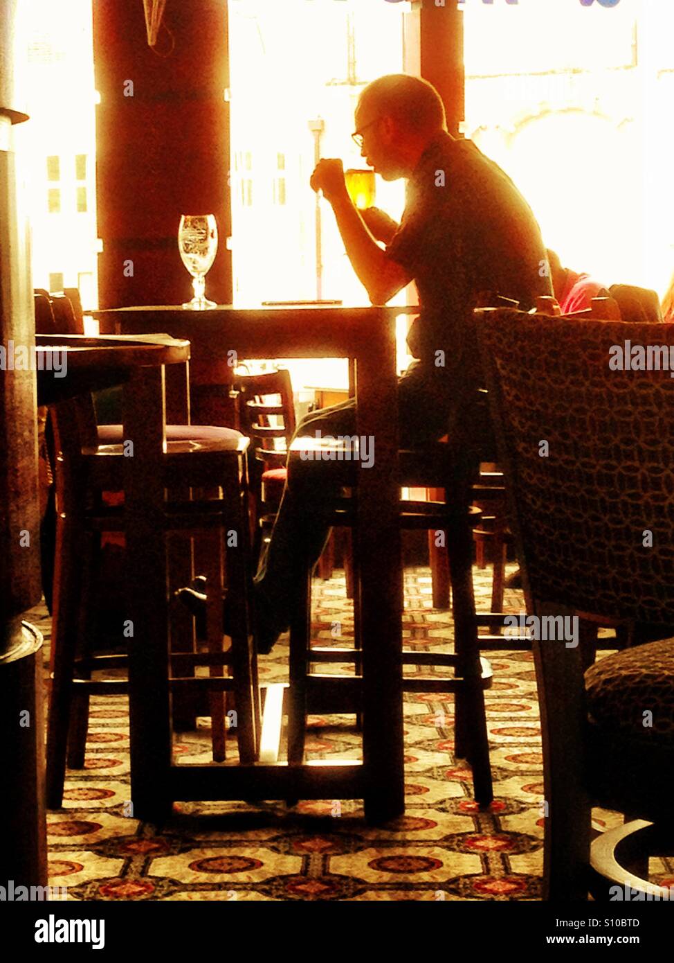 A man sits drinking alone in a bar. - Smartphone Captured Stock Image