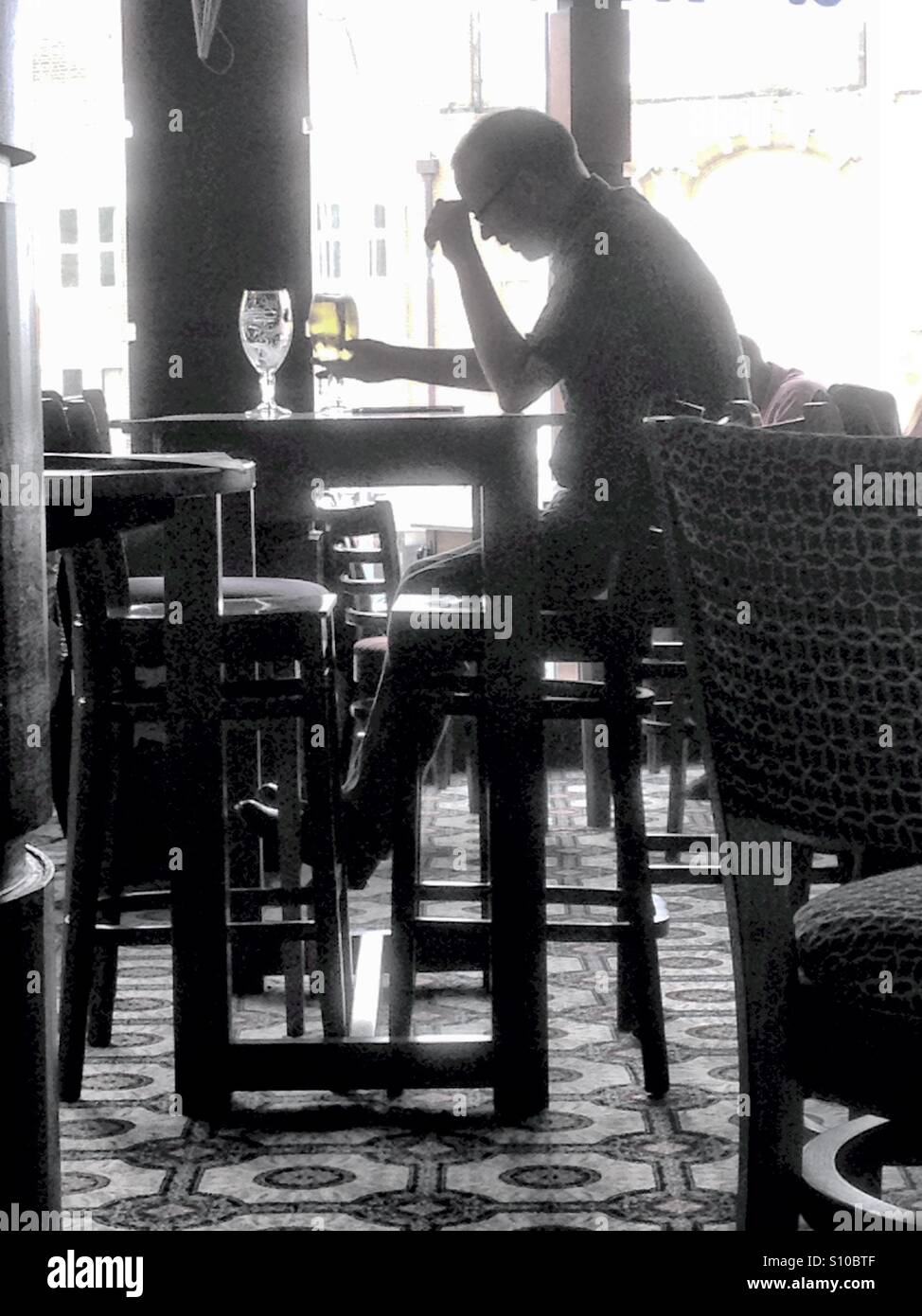 A man sits drinking alone in a bar. - Smartphone Captured Stock Image