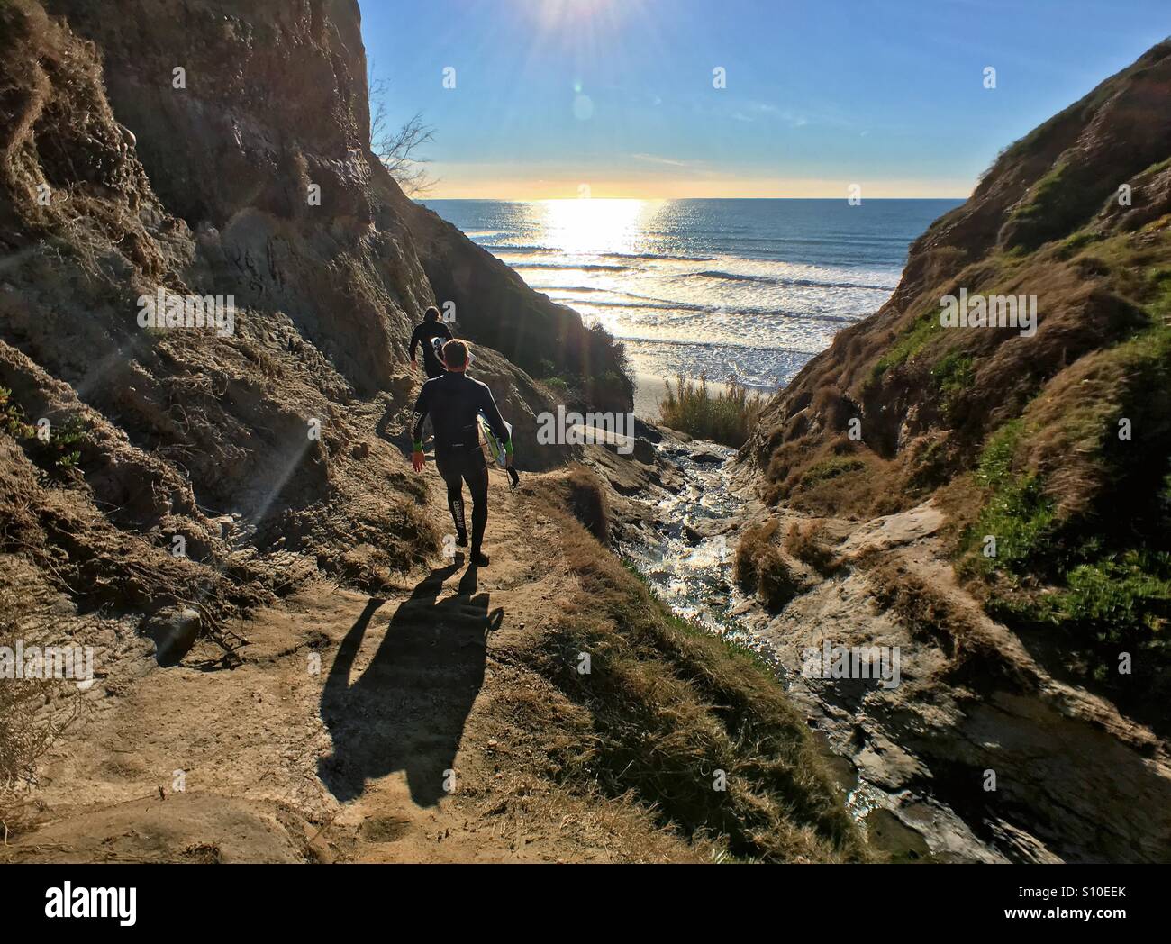 Two surfers hike along canyon to secret beach in La Jolla, California, USA. Taken 2 February 2016 Stock Photo