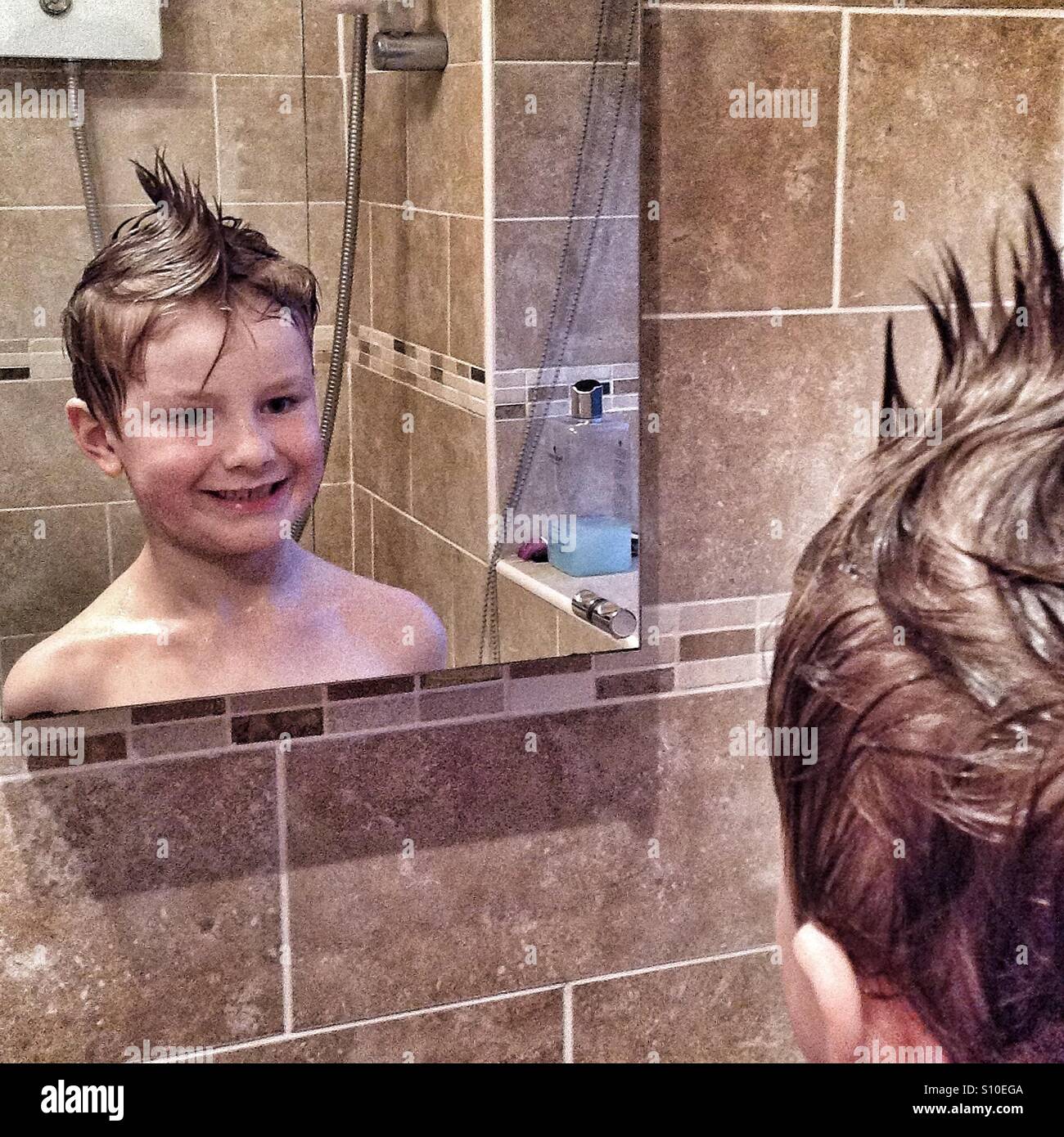 Boy looking into a bathroom mirror after playing with his hair in the bath Mohican style. Stock Photo